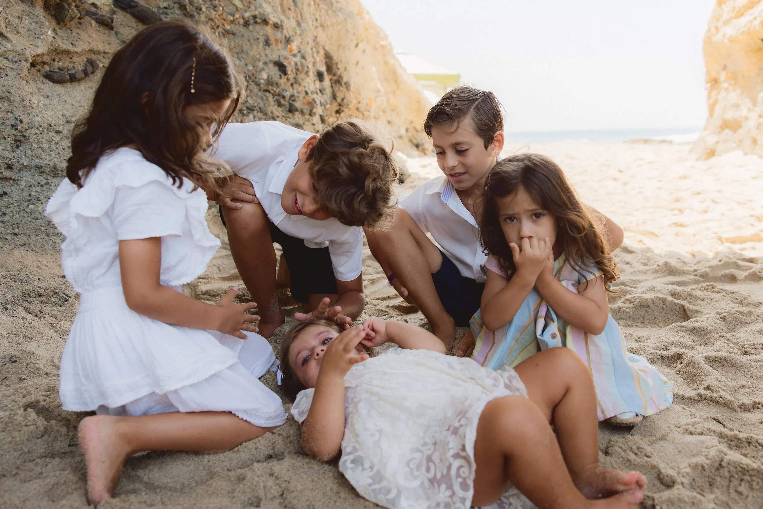 Three young siblings playing in the sand and laughing together at the base of the cliffs below the Montage Resort in Laguna Beach.