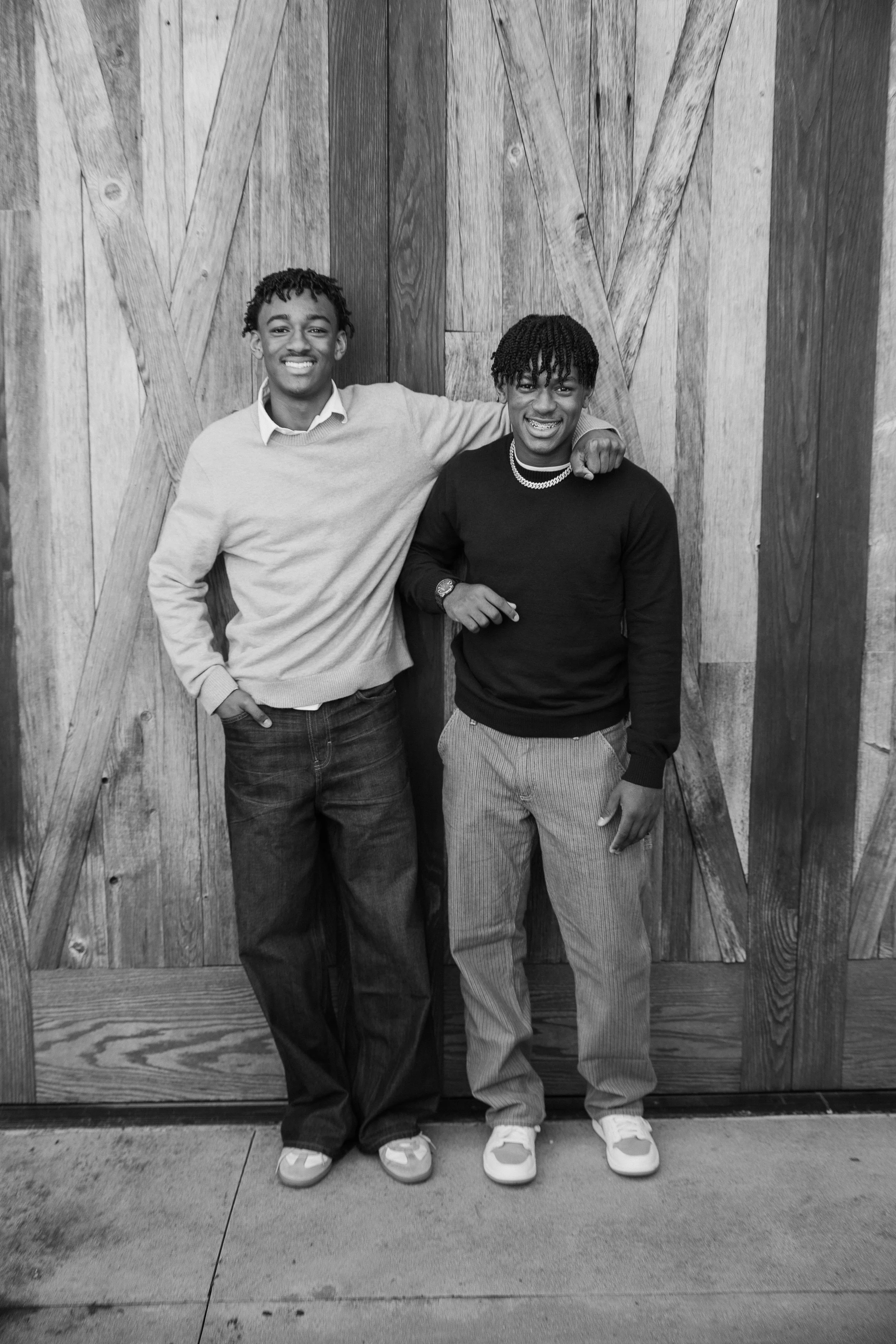 Black and white portrait of two brothers laughing and standing against a textured wooden barn door.