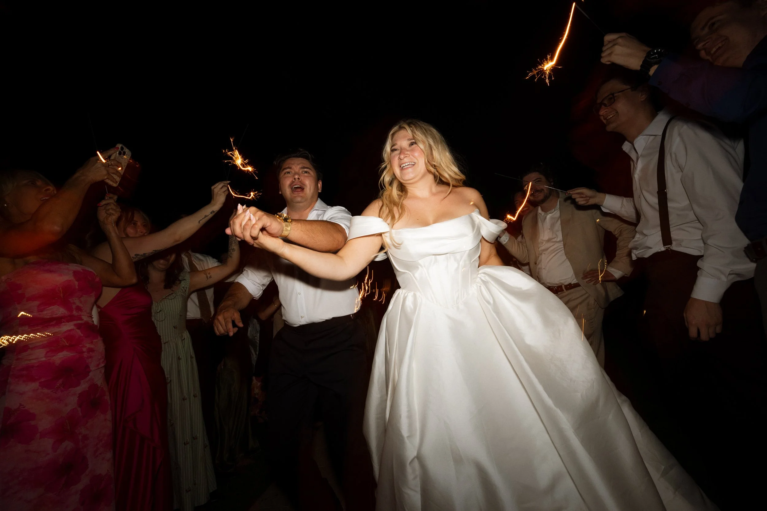 Bride and groom run hand in hand through a sparkler send-off