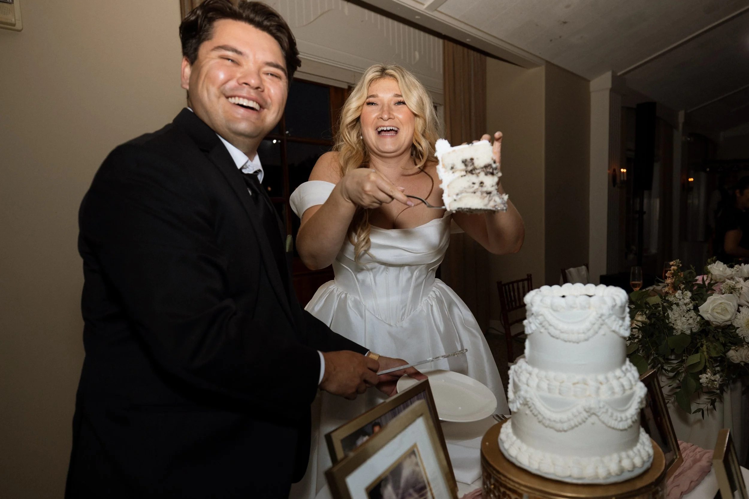 Bride holds up a slice of cake as she and the groom laugh