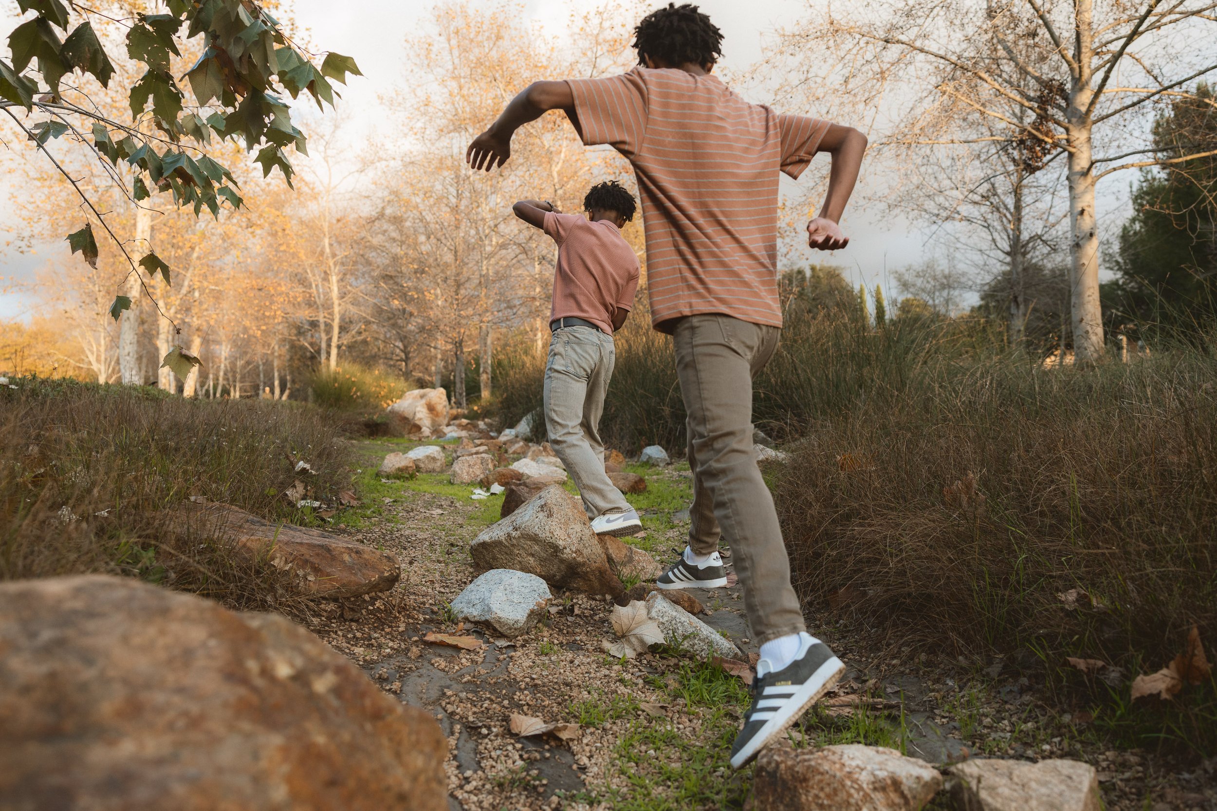 Two brothers jumping across large rocks and laughing during a playful family photo session at Jeffrey Open Space Trail in Irvine.