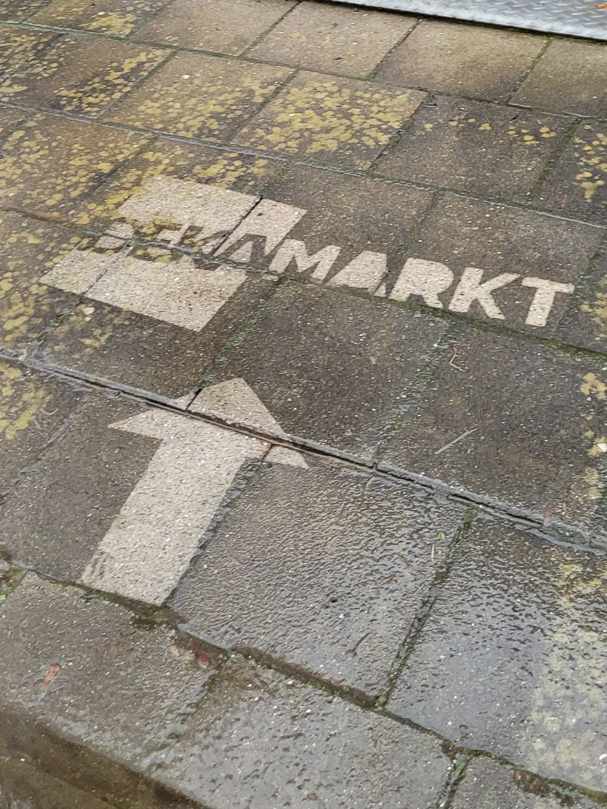 Een voetpad met witte markering die wijst richting een markt en een pijl die naar links wijst.