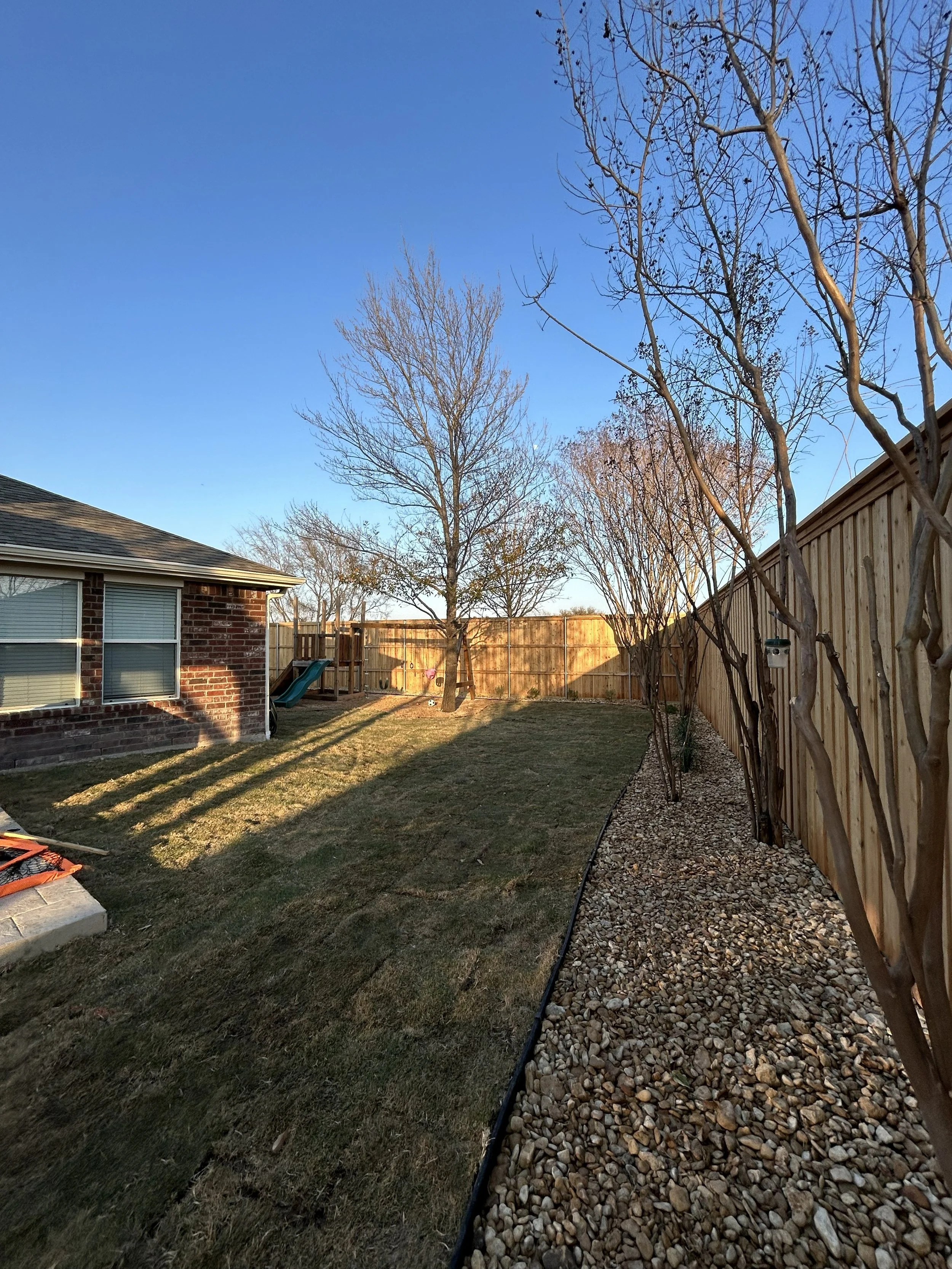 After photo showcasing results of landscape installation with new grass, gravel, and plants