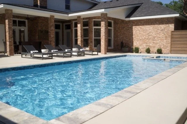 Outdoor pool area with modern lounge chairs, brick house in background