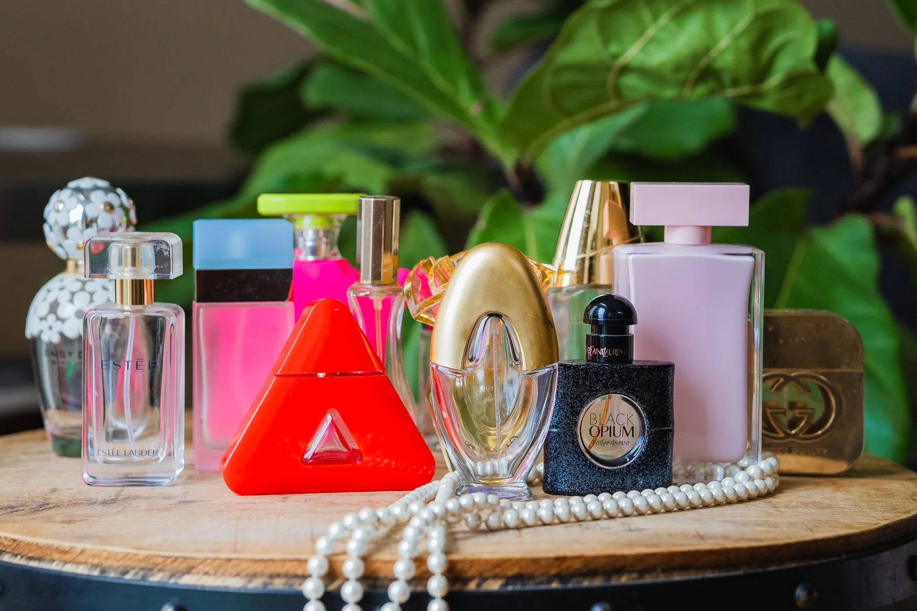 Assorted perfume bottles displayed on a wooden surface with a string of pearls.