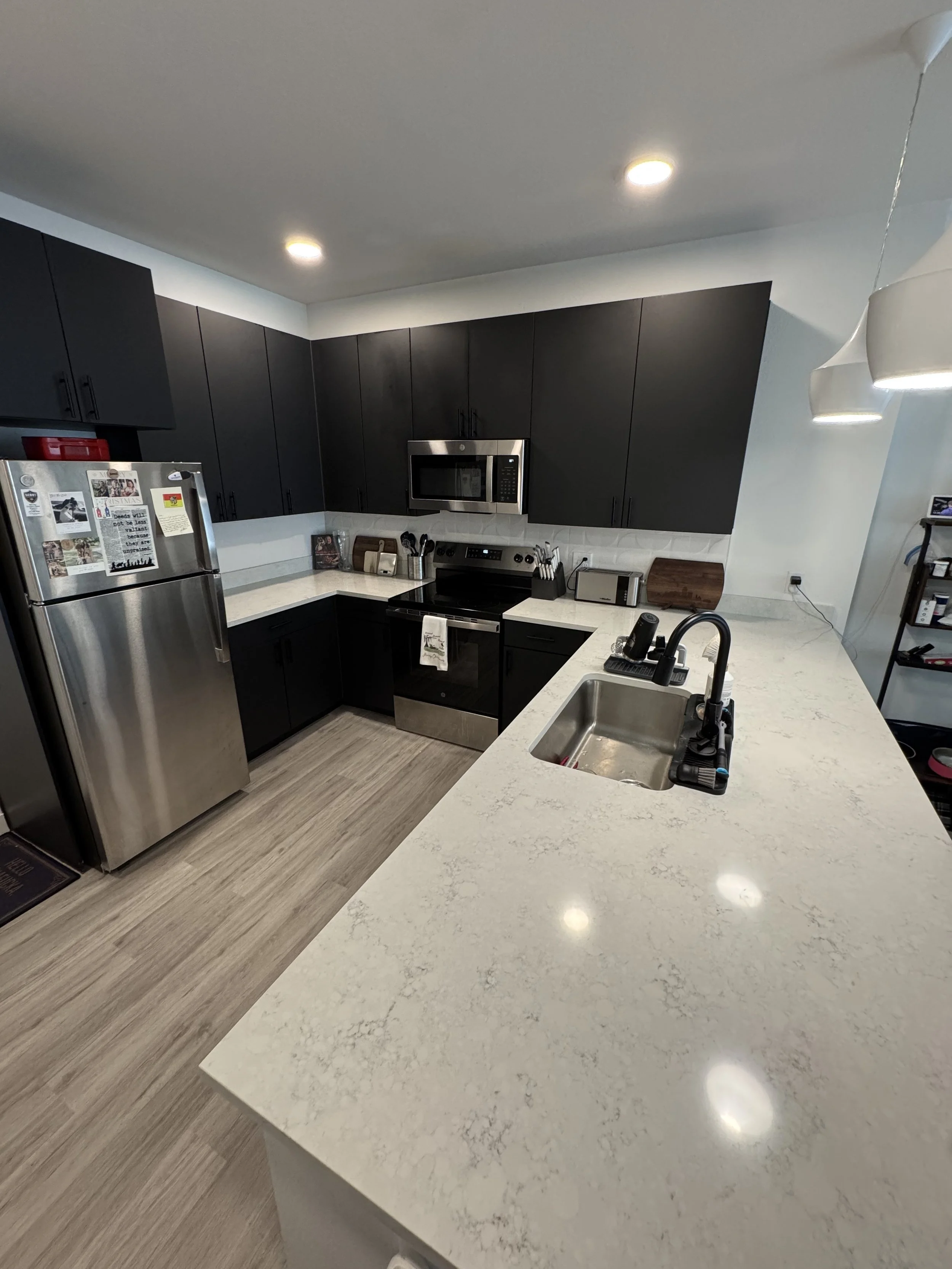 Modern kitchen with stainless steel appliances, white cabinets, black tile backsplash, and white island with black stools