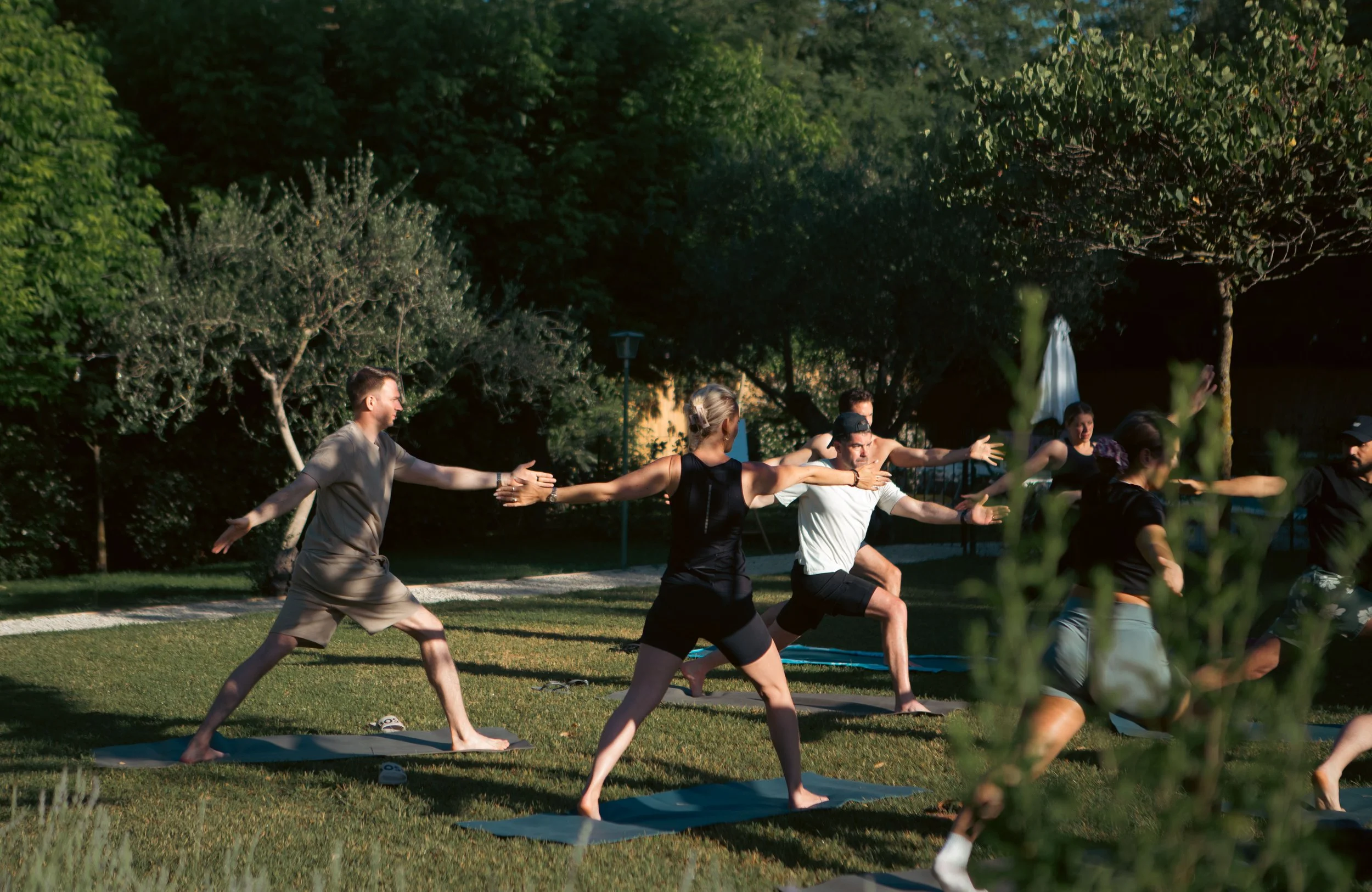 Group of people practicing yoga outdoors in a park with trees.