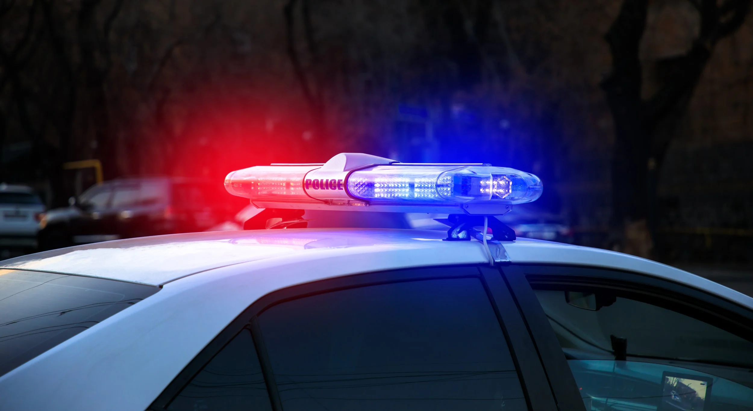 Police car with red and blue emergency lights flashing, parked outdoors in a dark area.