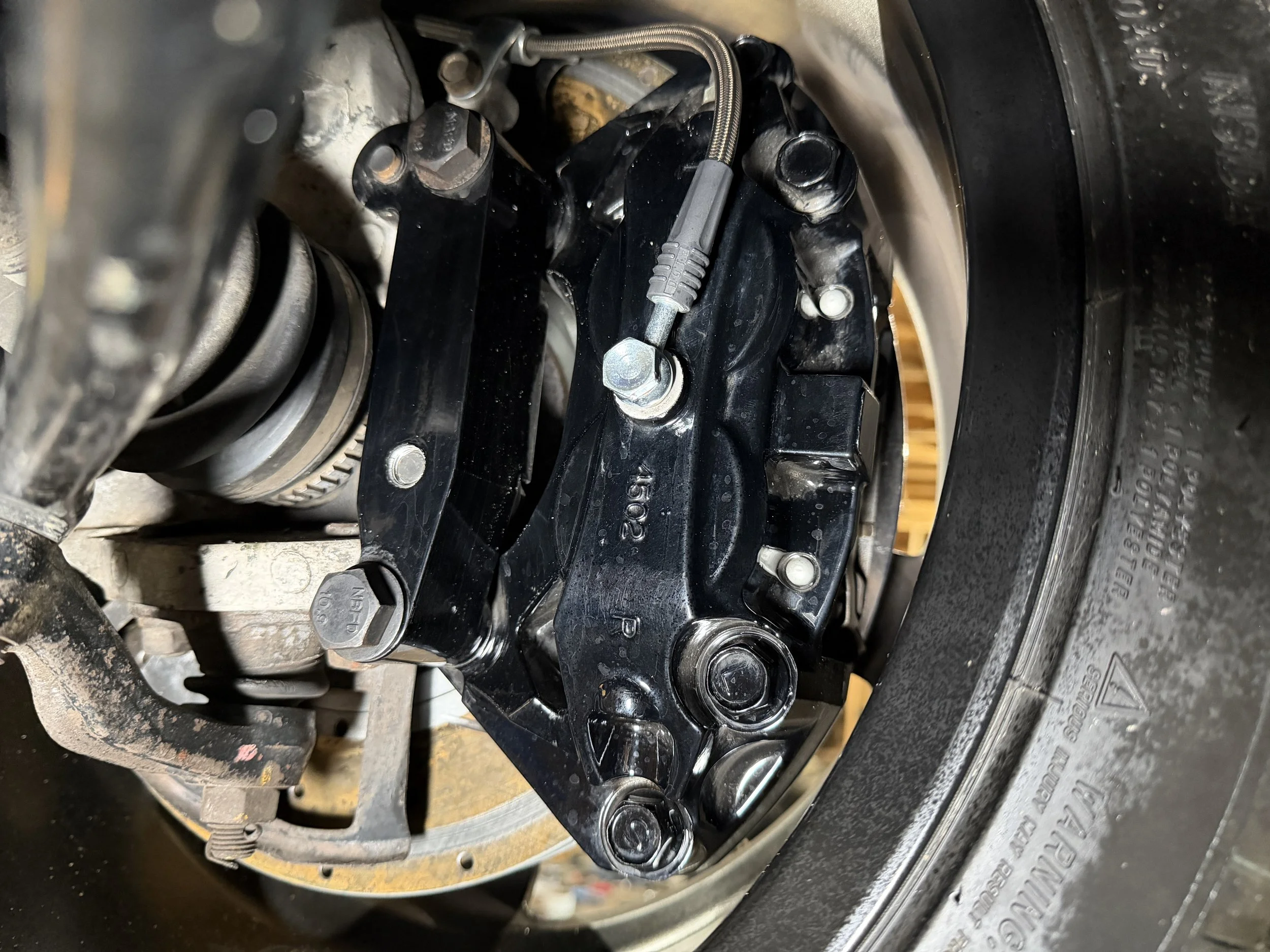 Close-up view of a motorcycle front wheel assembly, showing the brake caliper, suspension components, and tire.