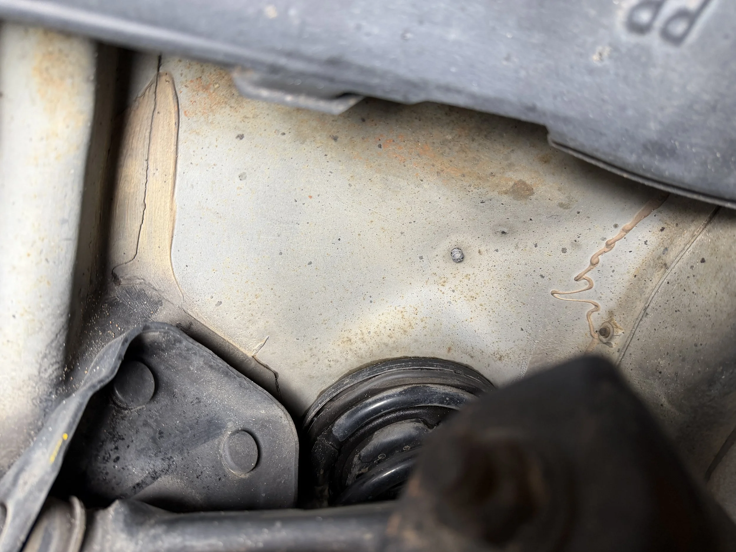 Close-up view of the underside of a vehicle showing a coil spring, metal parts, and some rust and dirt.
