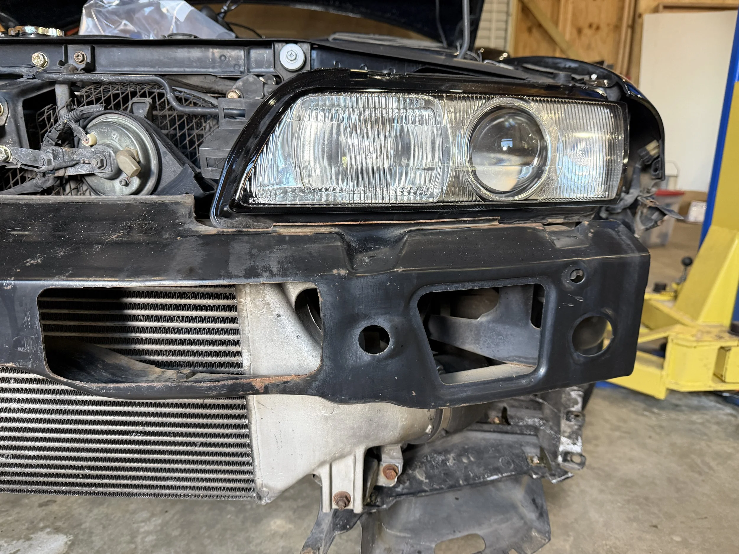 Close-up of the front of a car with the bumper removed, showing the headlight, radiator, and internal components.