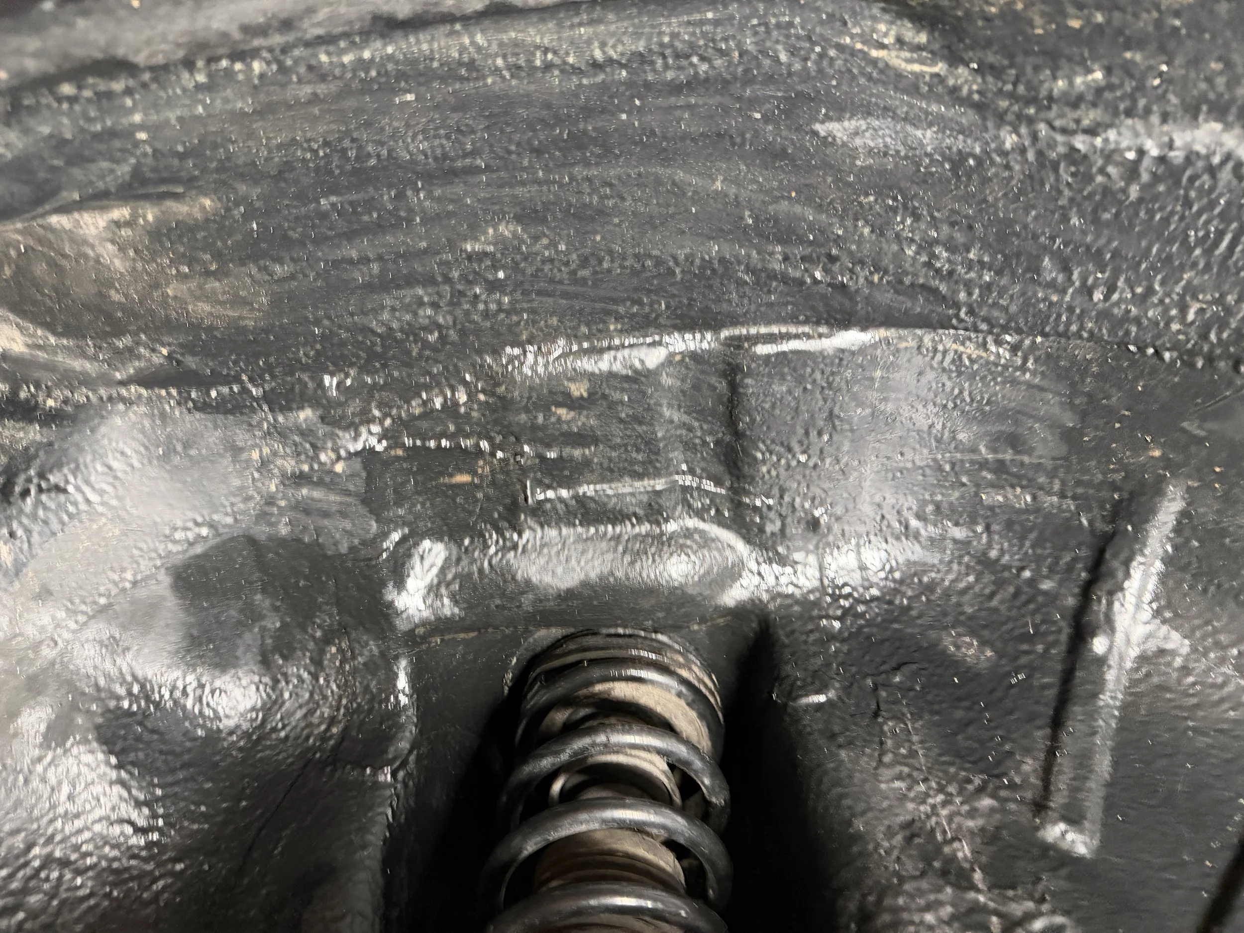 Close-up of a metal spring and textured black surface, possibly part of a mechanical device or machinery.