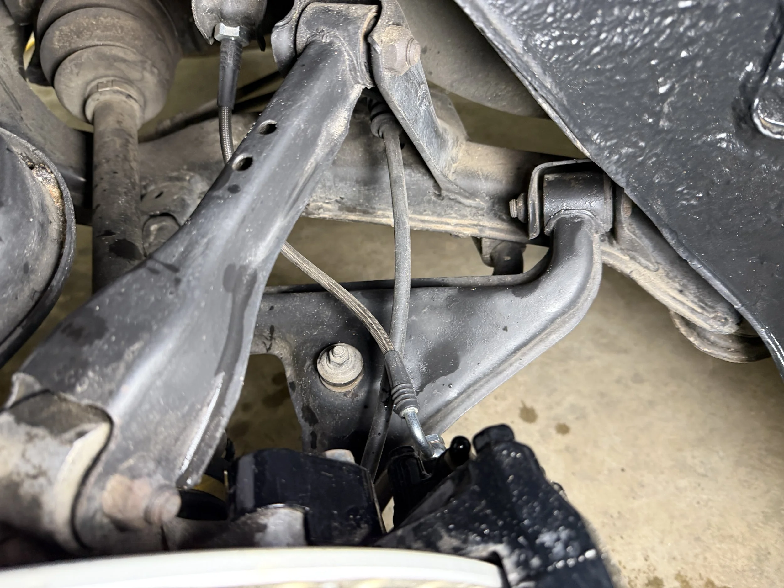 Close-up of a car's suspension and steering components, including a control arm, bolt, and metal rods, with some dirt and grease visible.