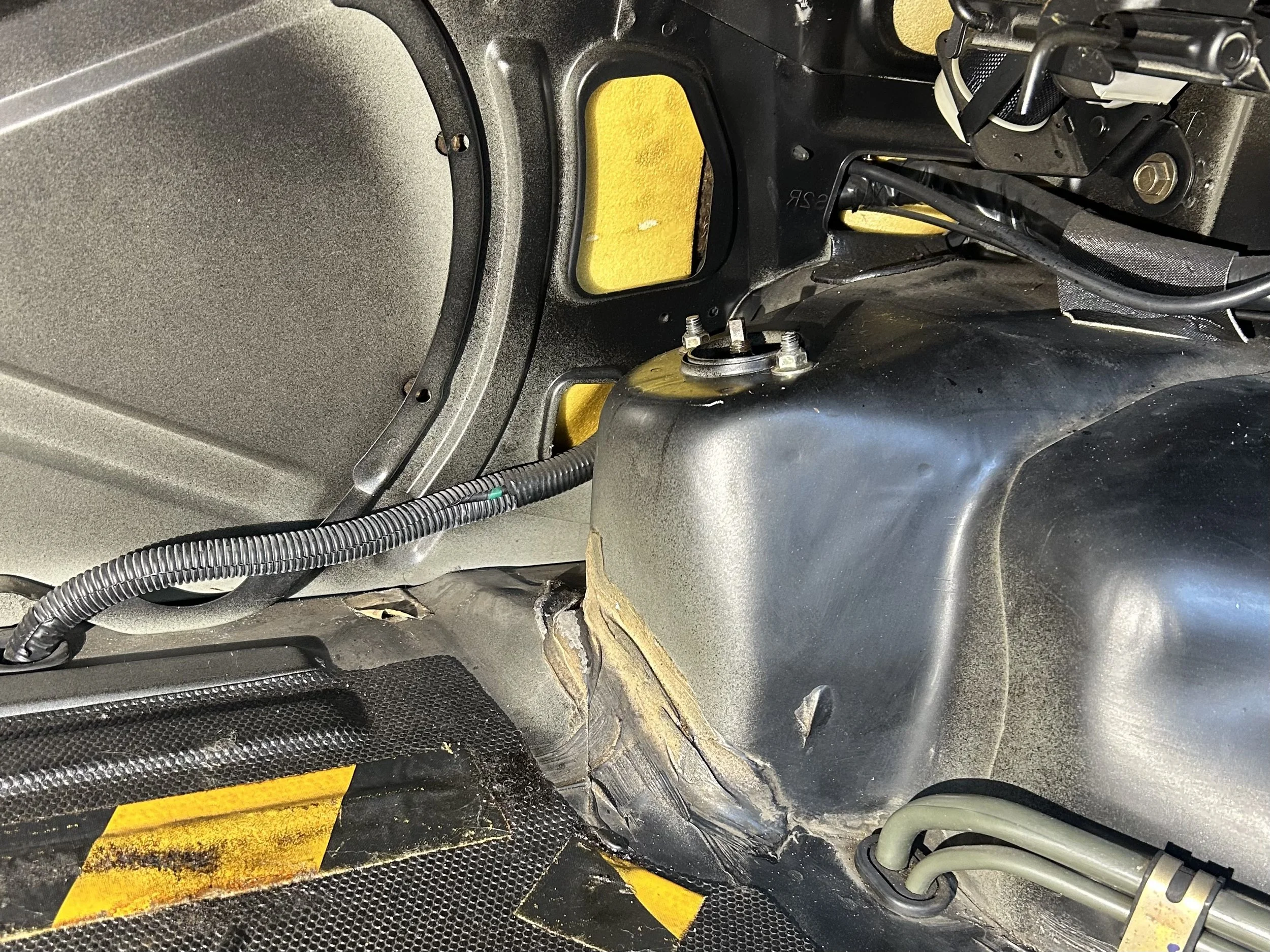 Interior of a vehicle showing the floor and side panels with wiring and a black plastic container, possibly part of the vehicle's mechanical or electrical system.