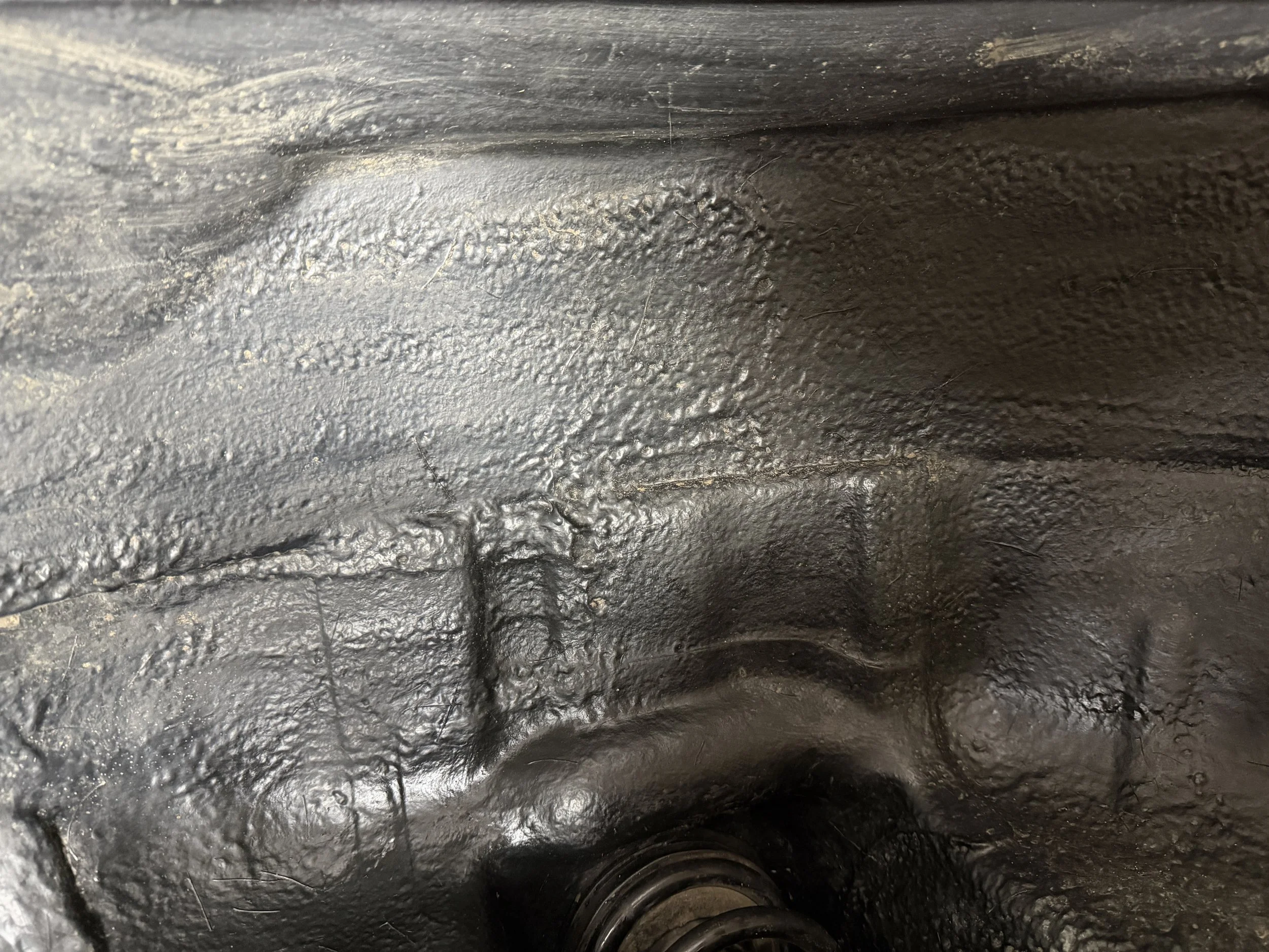 Close-up of a textured black metal surface, possibly part of machinery or engine, with some scratches and a bolt at the bottom.
