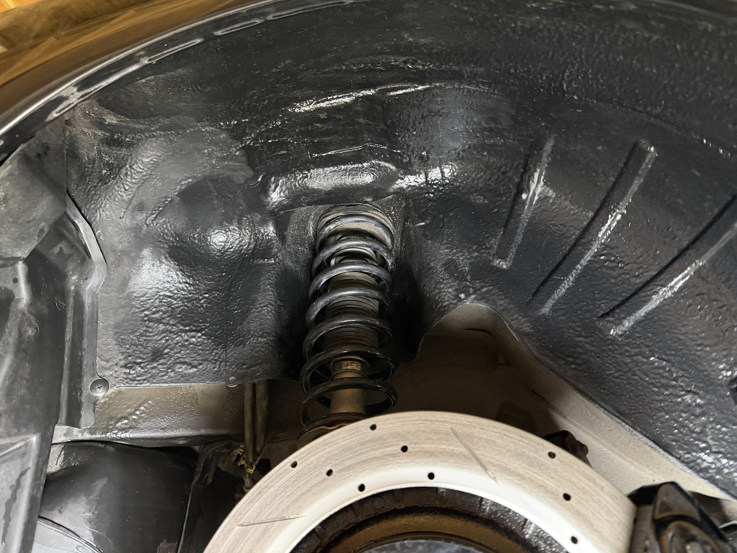 Close-up of a black-painted car suspension system, showing a coil spring and parts of the brake rotor.