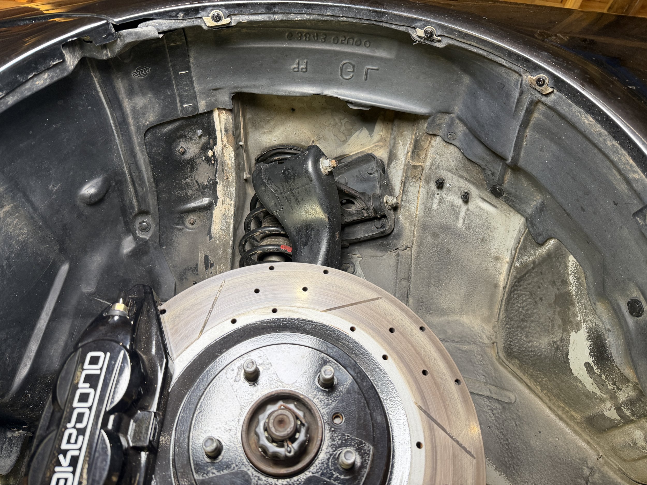 Close-up view of a car's wheel well with a brake rotor, part of a suspension system, and brake caliper visible.