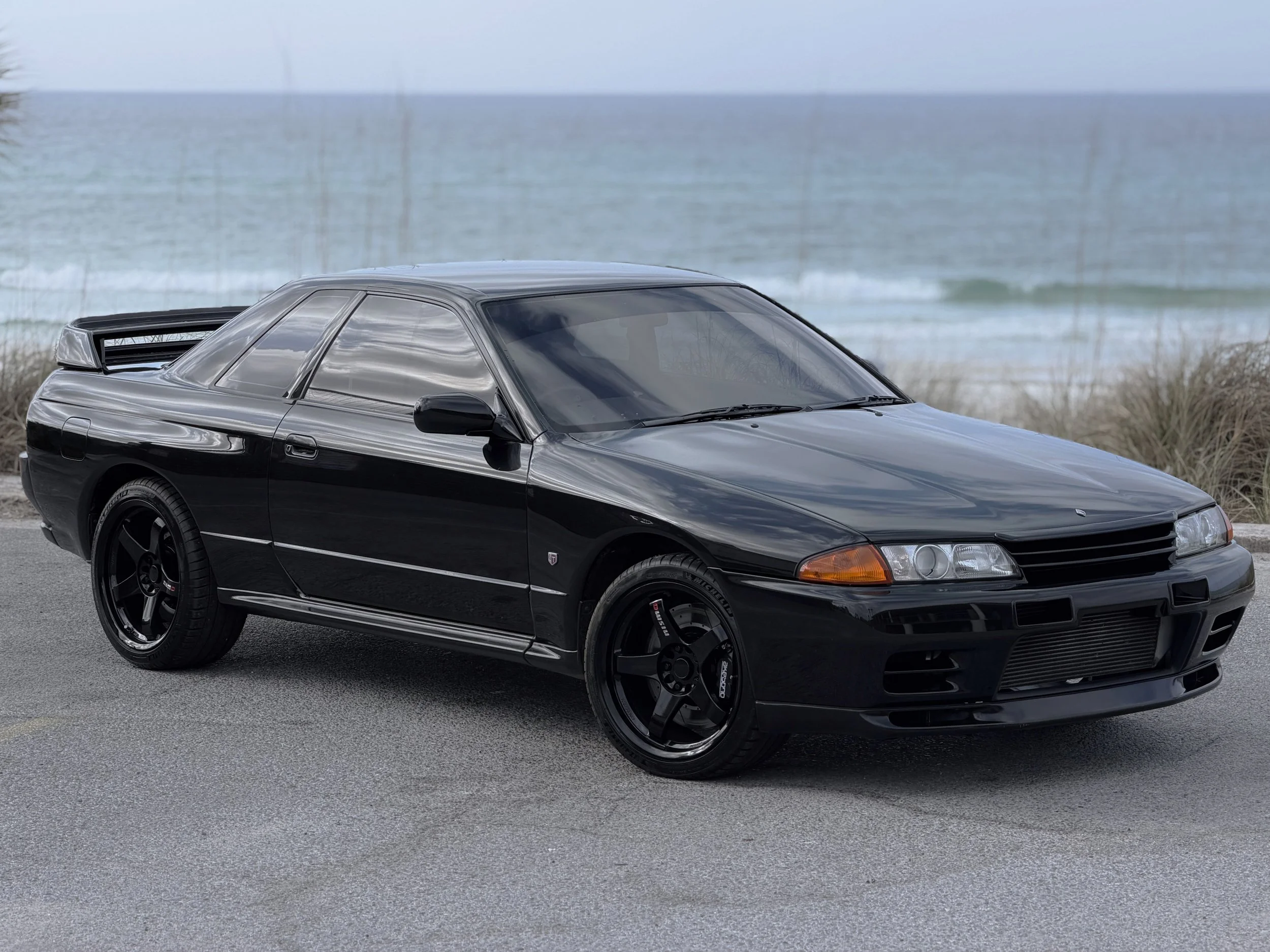 Black sports car parked near the beach with ocean in the background.