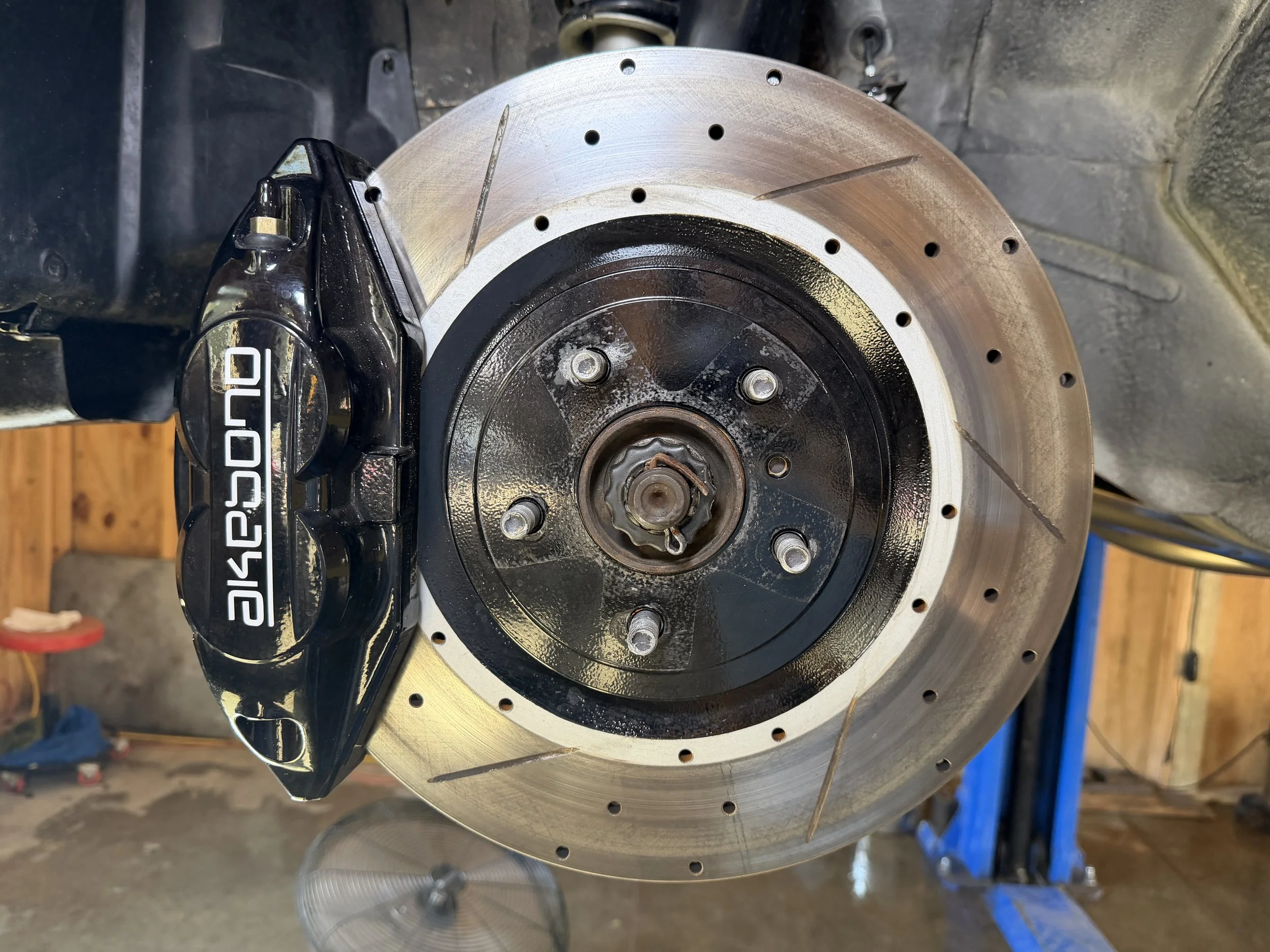 Close-up of a car brake system with a large, ventilated brake rotor, black wheel hub, and a black Brembo brake caliper with white lettering.