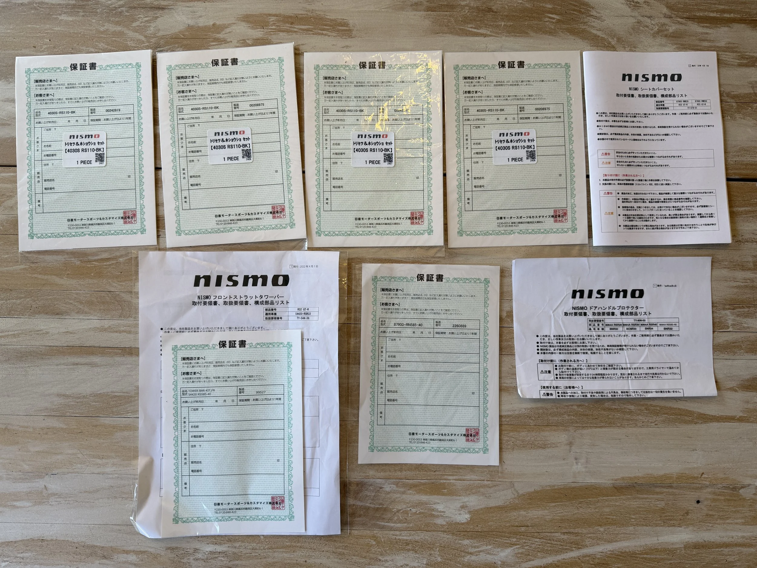 Several Nismo warranty documents and instruction manuals, some sealed in plastic, are arranged on a wooden surface.