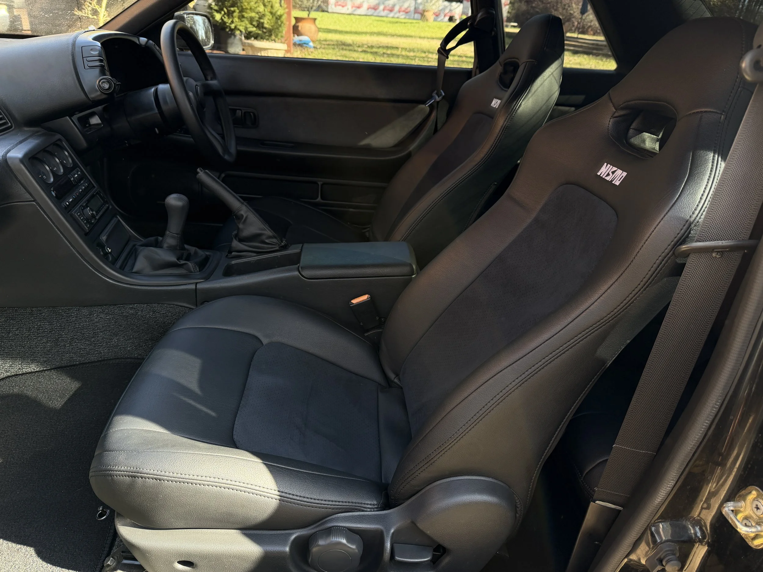 The interior of a car showing black racing seats with the Nissan logo, a gear shifter, and the dashboard with the steering wheel.