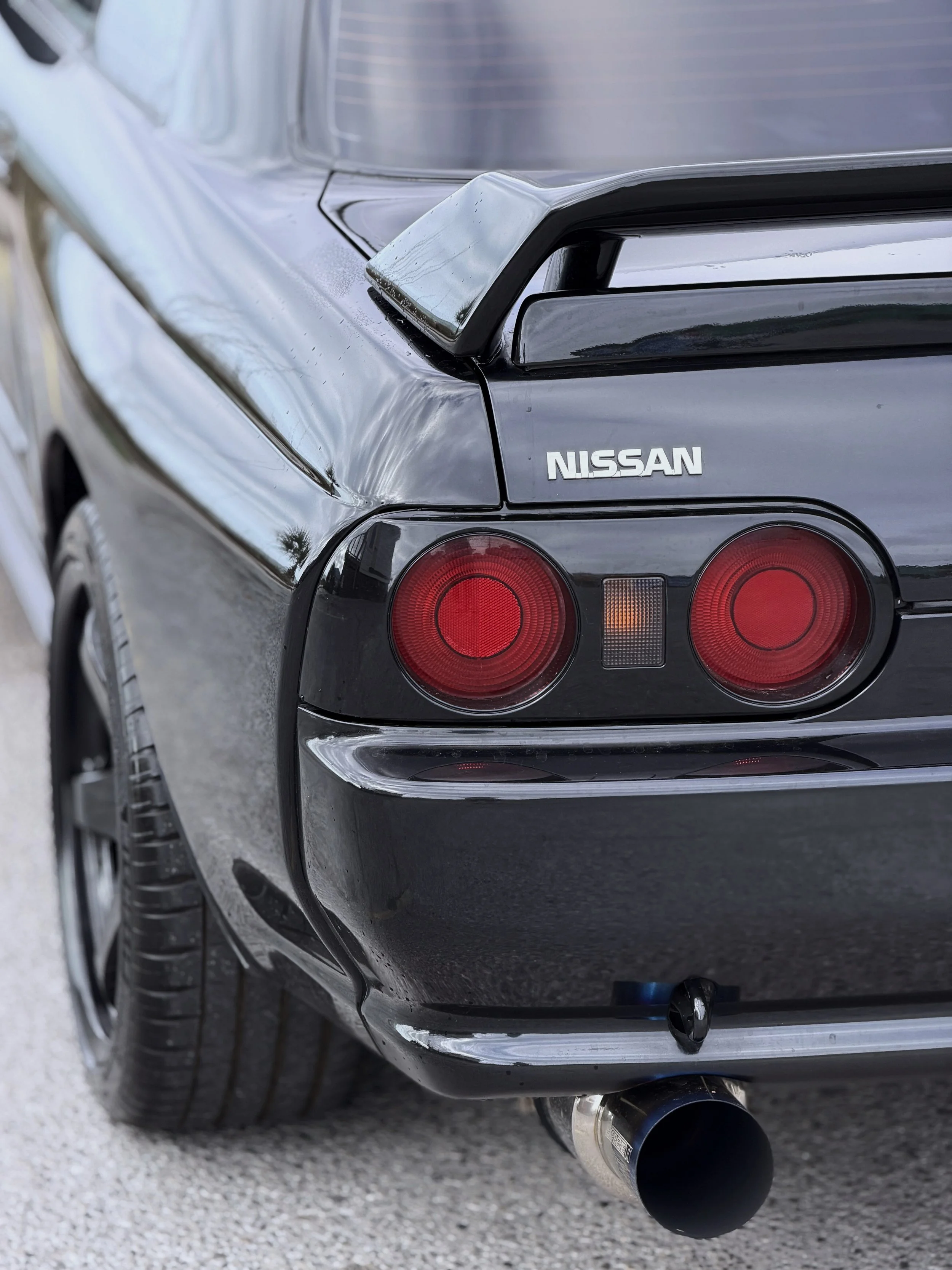 Close-up of the rear end of a black Nissan car showing the tail light, rear bumper, and exhaust pipe.
