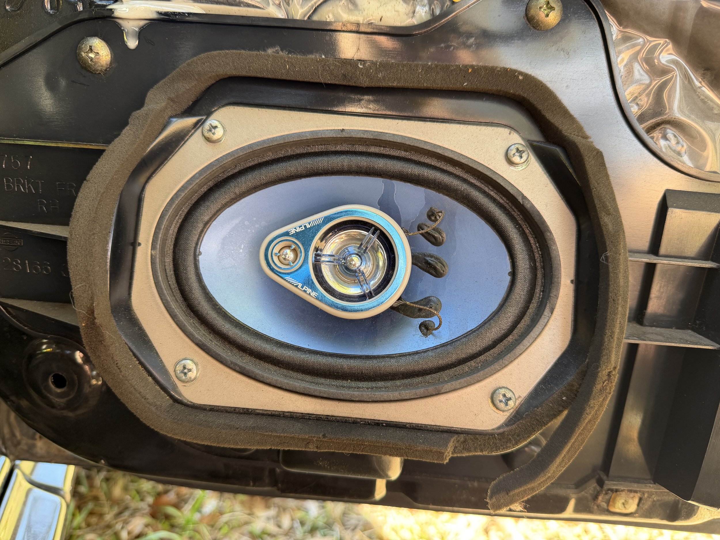 Close-up view of a car speaker with a blue surround, mounted inside a black enclosure with screws, and some foam padding around the edges.