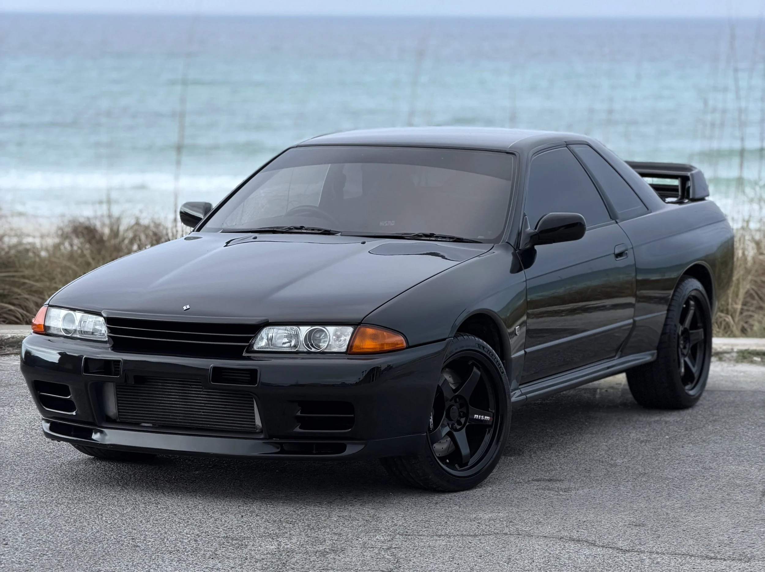 A black sports car parked on a road near a body of water with a cloudy sky in the background.