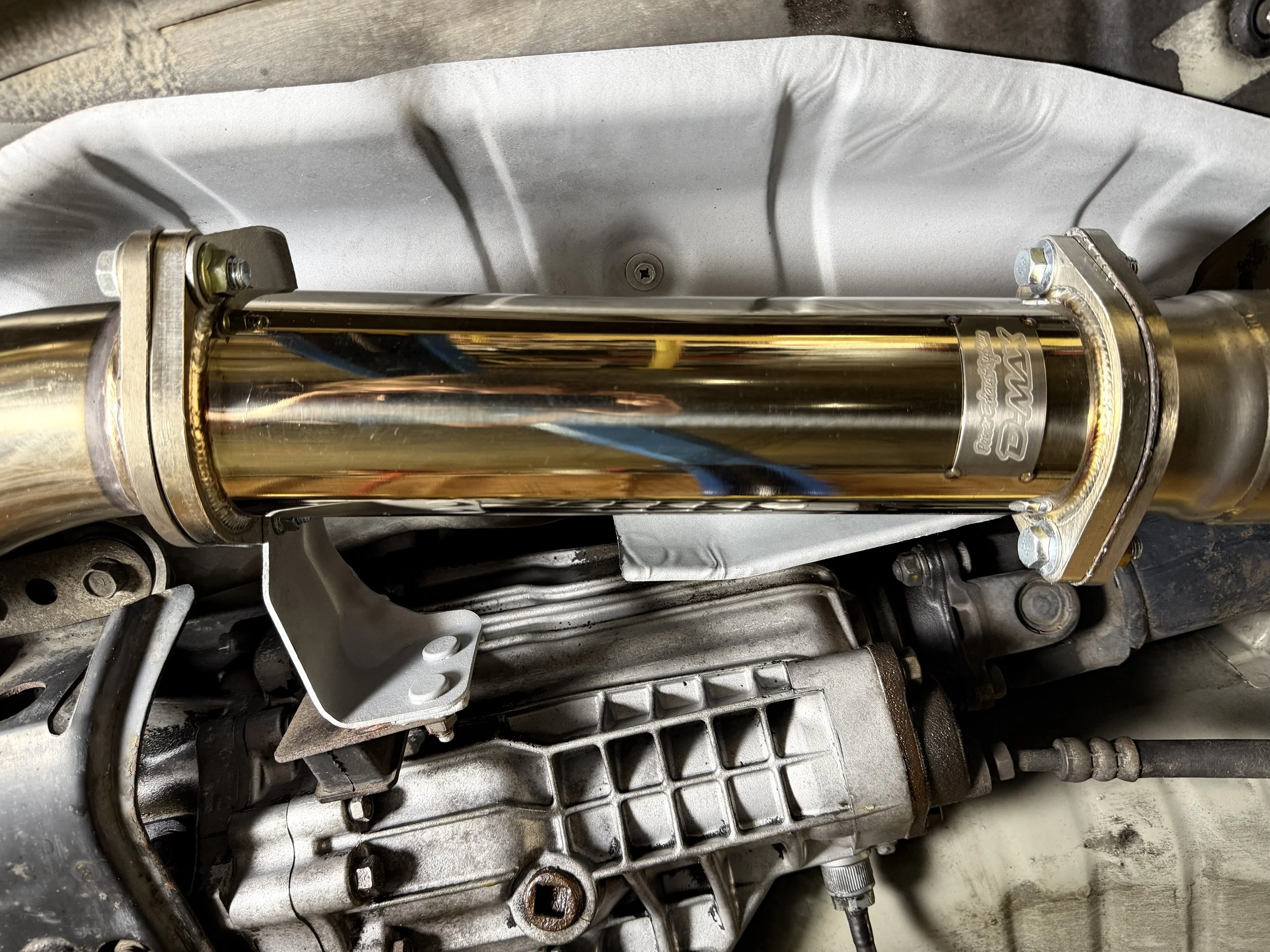 A close-up view of a shiny, bronze-colored automotive component with bolts and a couple of cables attached, mounted on a metallic engine part.