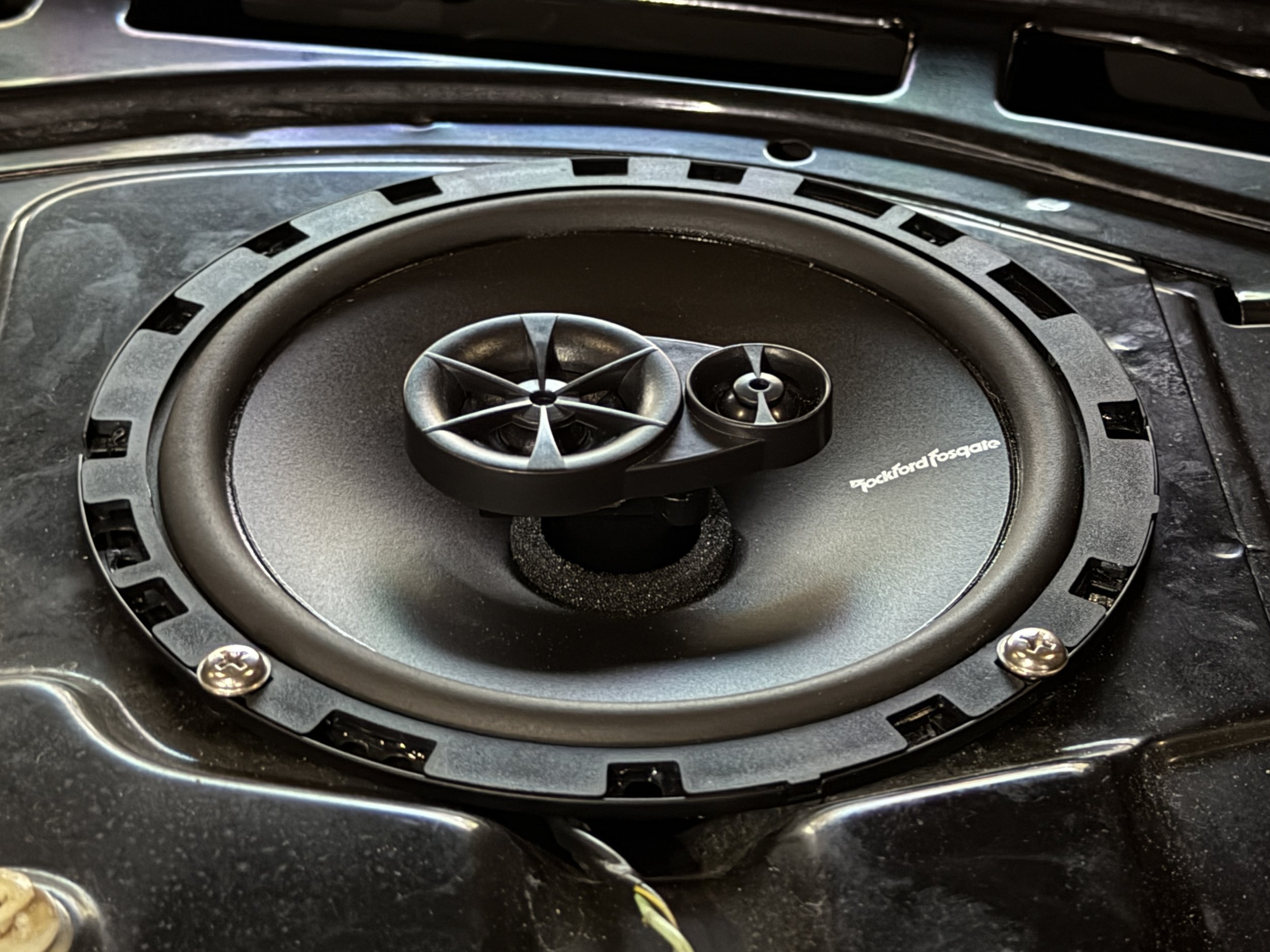 Close-up of a car speaker with a black cone and a smaller tweeter in the center, mounted in a black housing.