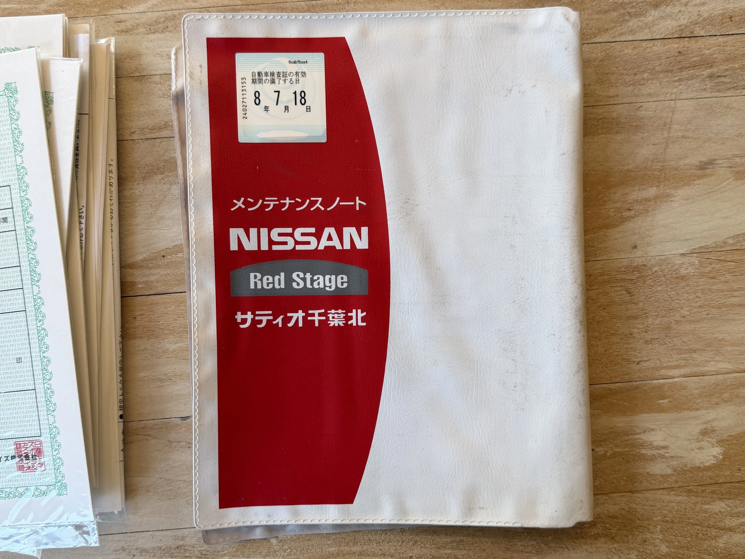 Nissan maintenance note with red and white cover, labeled 'Red Stage' in English and Japanese, placed on a wooden surface.
