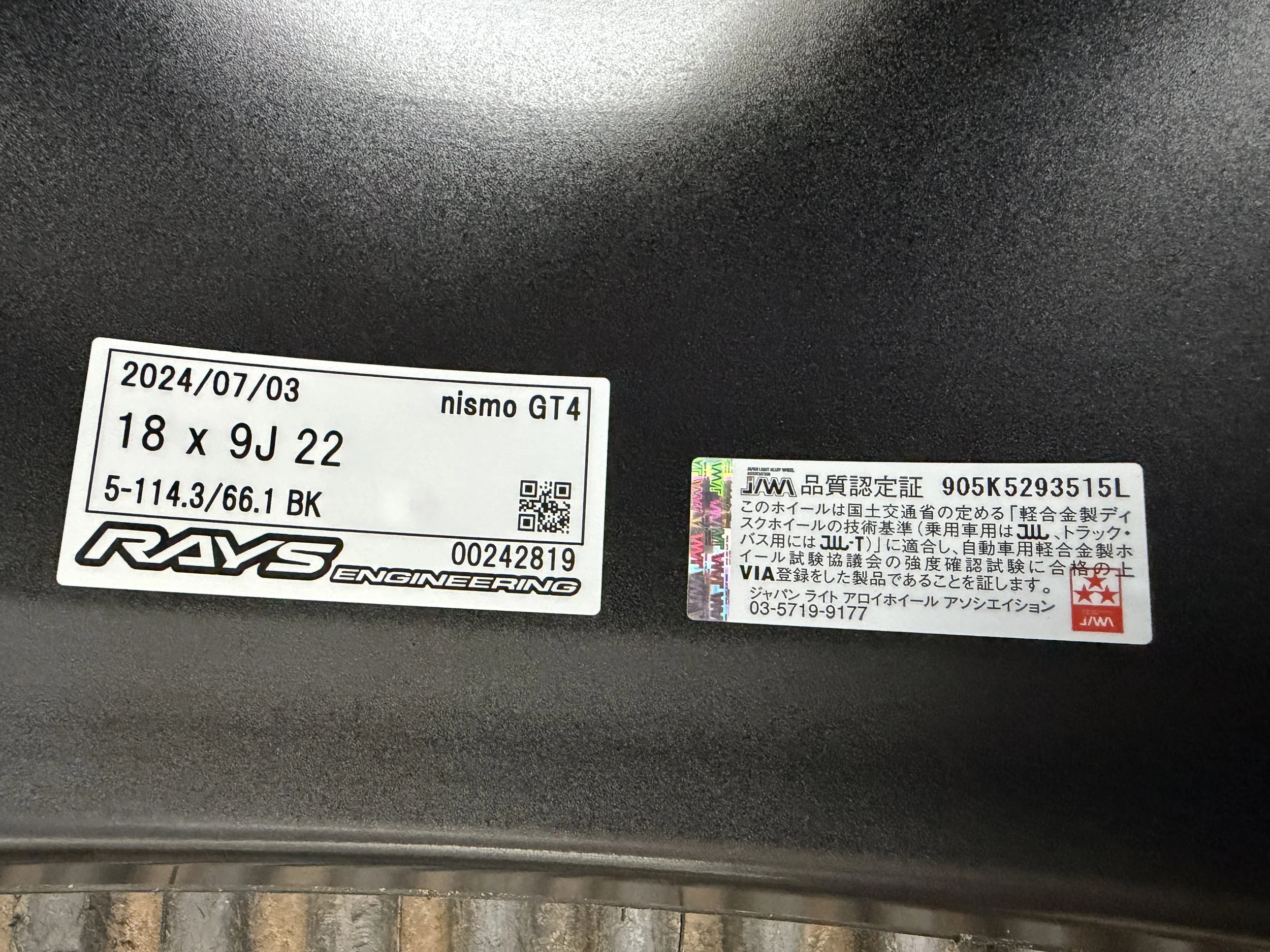Close-up of two tire labels on a black tire, one from RAYS Engineering with details about the tire model nismo GT4, size 18 x 9J 22, and another from JWA with Japanese text and certification marks.