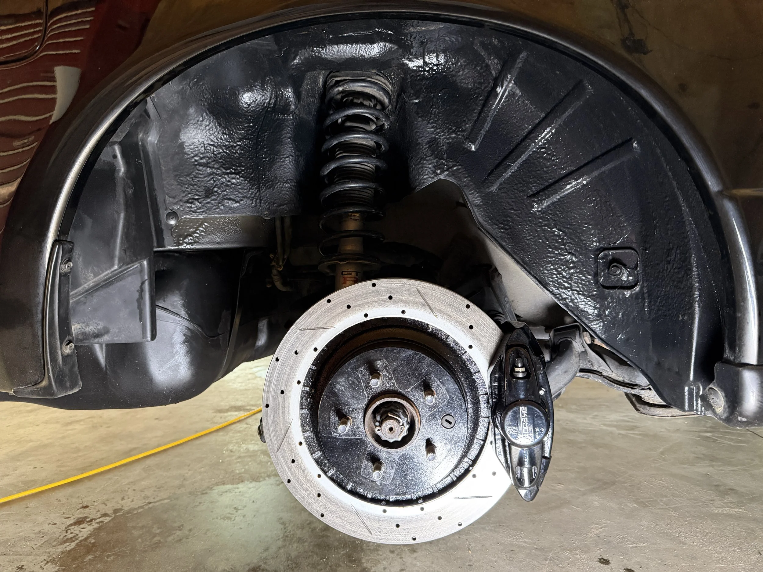 Close-up of a motorcycle's front wheel assembly with an exposed brake disc, suspension system, and wheel hub, with the wheel removed.