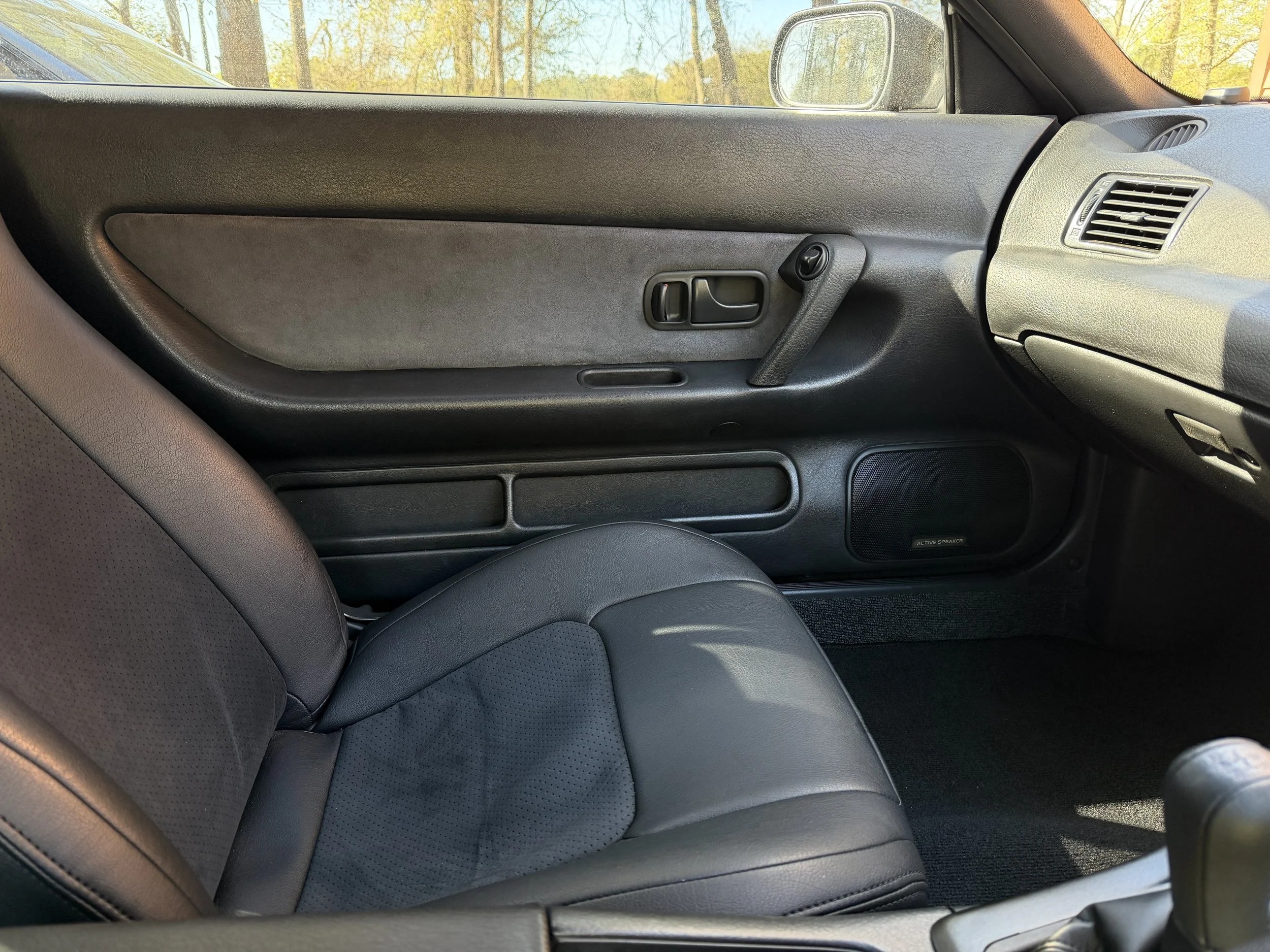 Interior of a car showing the passenger side door, black leather seat, dashboard, and air vent.