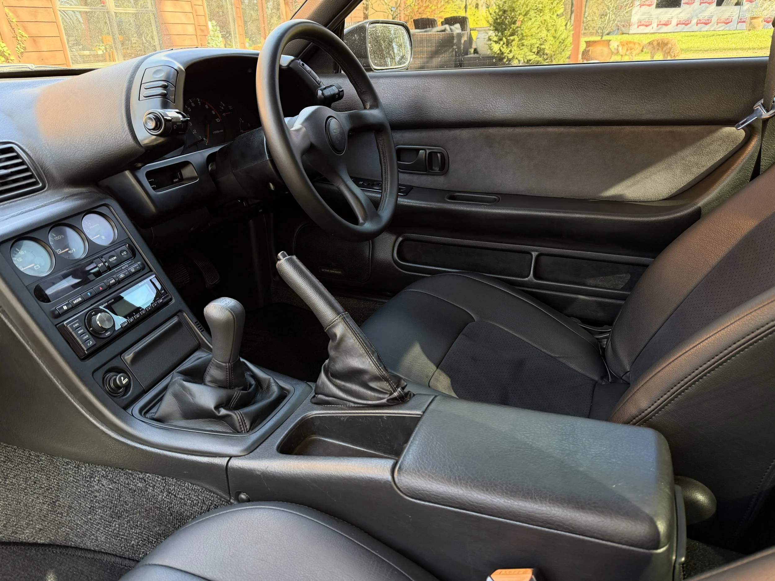 Interior of a car showing the driver's side, including the steering wheel, dashboard with gauges, gear shift, and the front seat with a seatbelt.