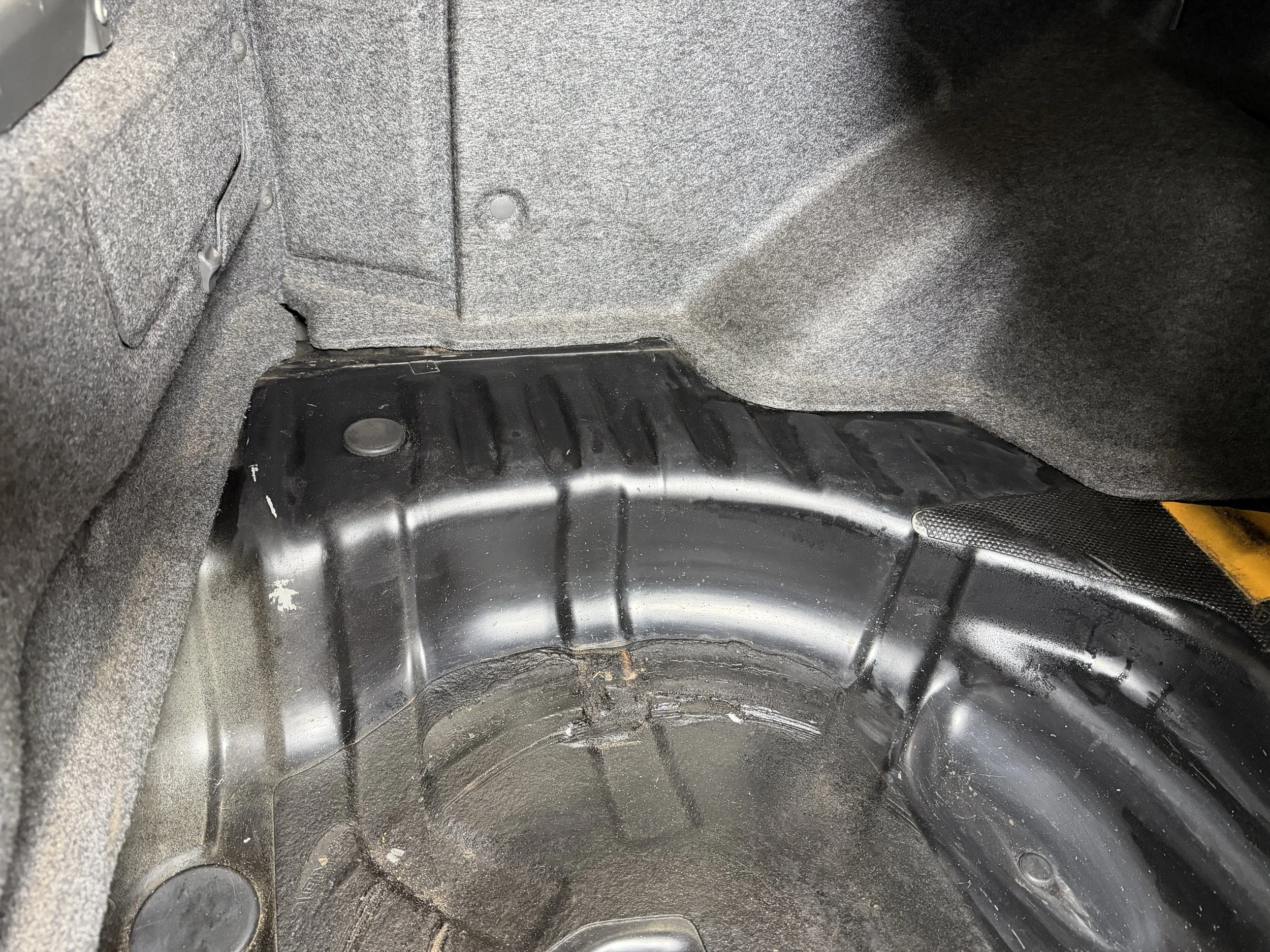 Empty car trunk with black painted metal surface and gray carpeted lining.