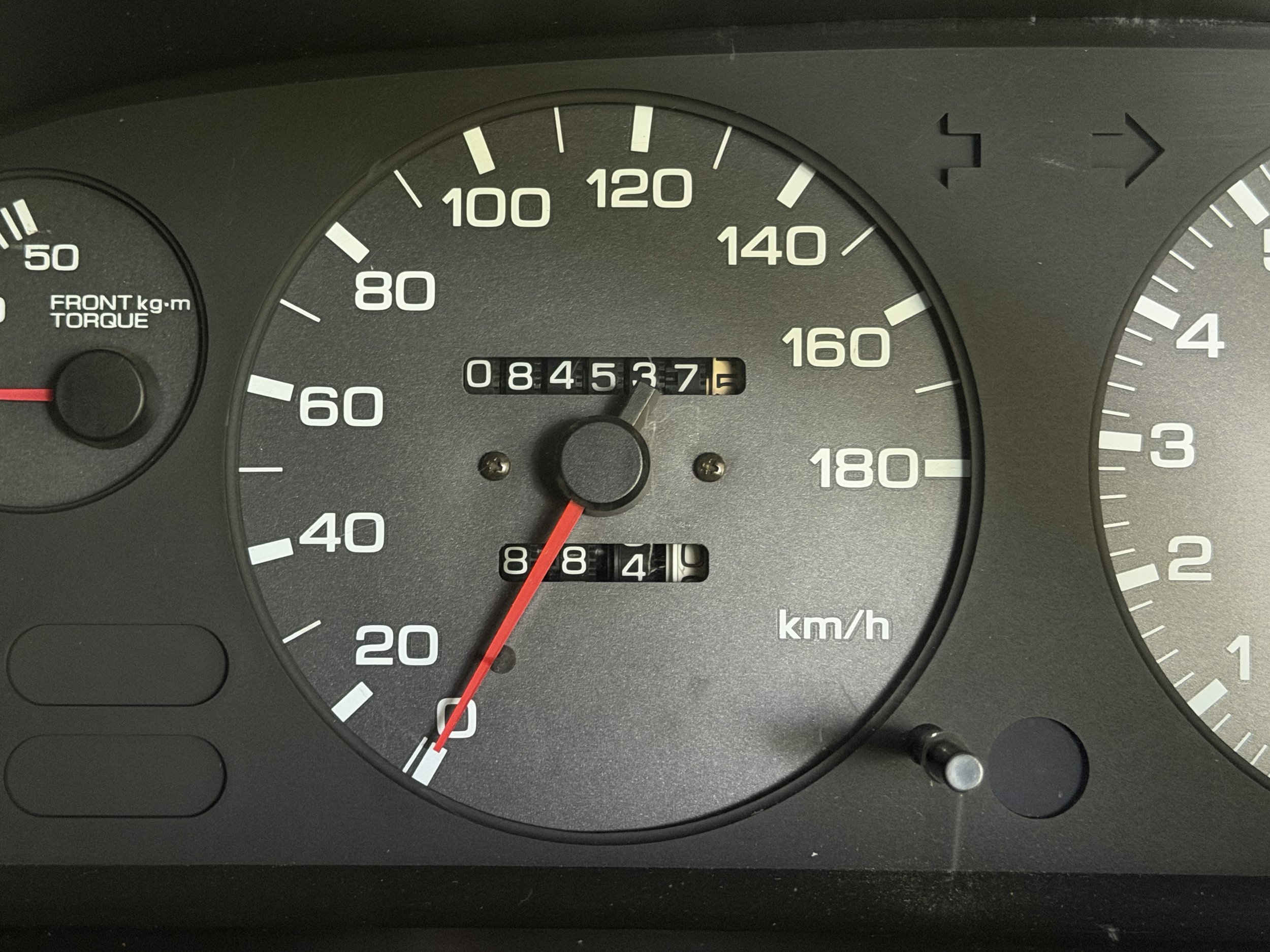 A car dashboard showing an odometer reading 84,537.3 kilometers, a speedometer indicating 0 km/h, and a tachometer showing around 800 RPM.