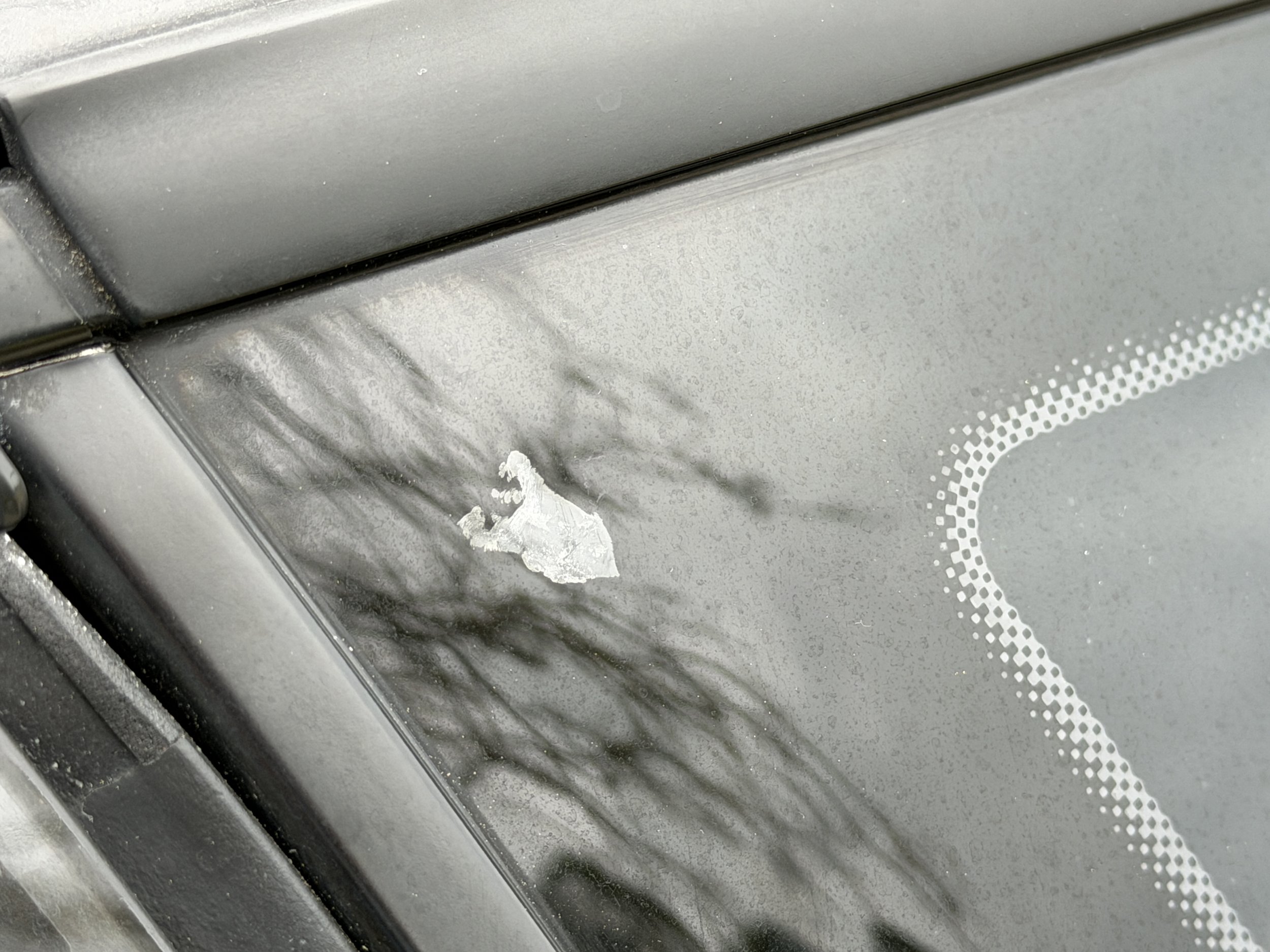 Close-up of a car windshield with a scratch and peeling paint near the top edge.
