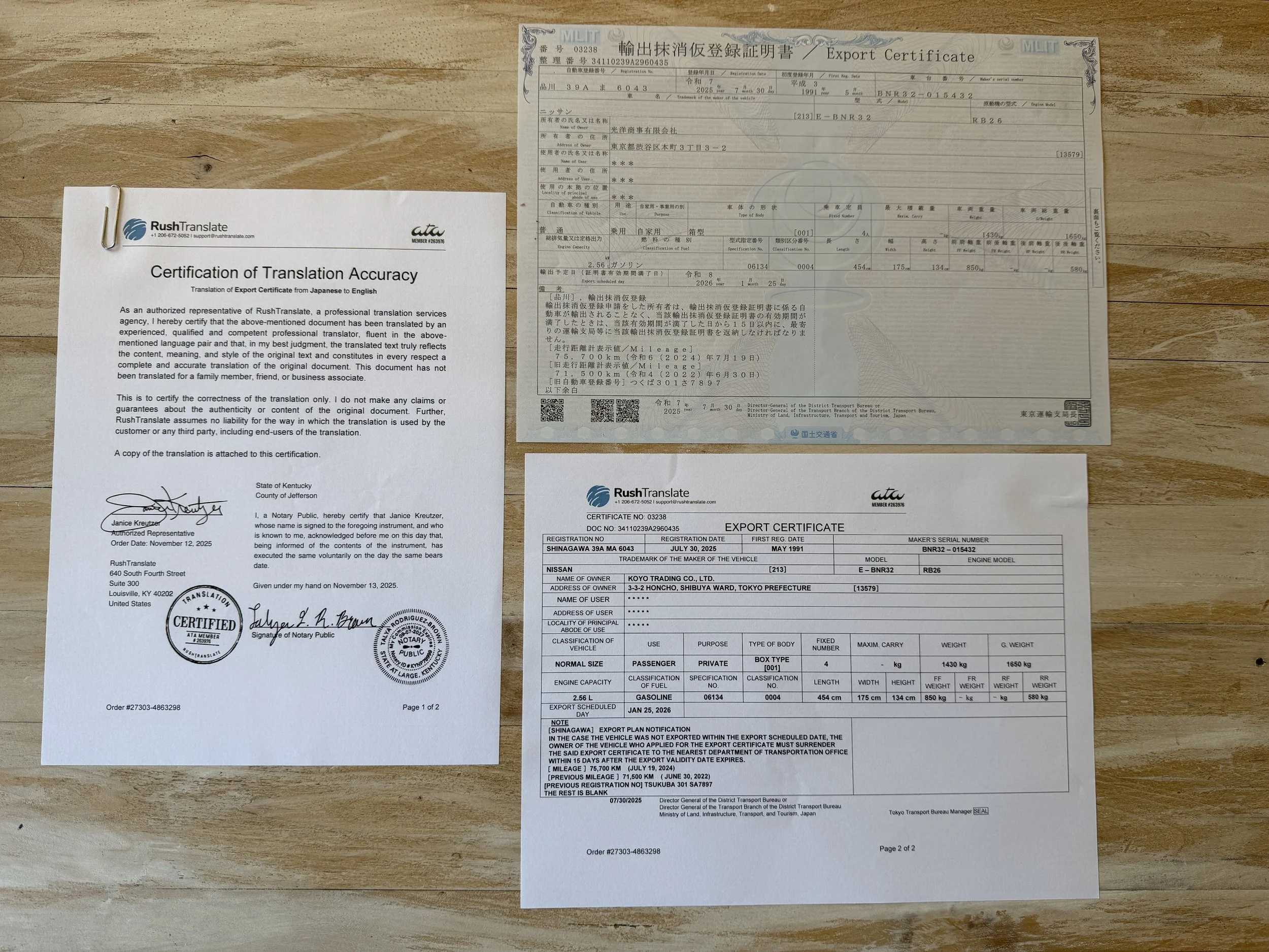 Collection of documents including an export certificate, a translation certification, and a Japanese export form laid out on a wooden surface.