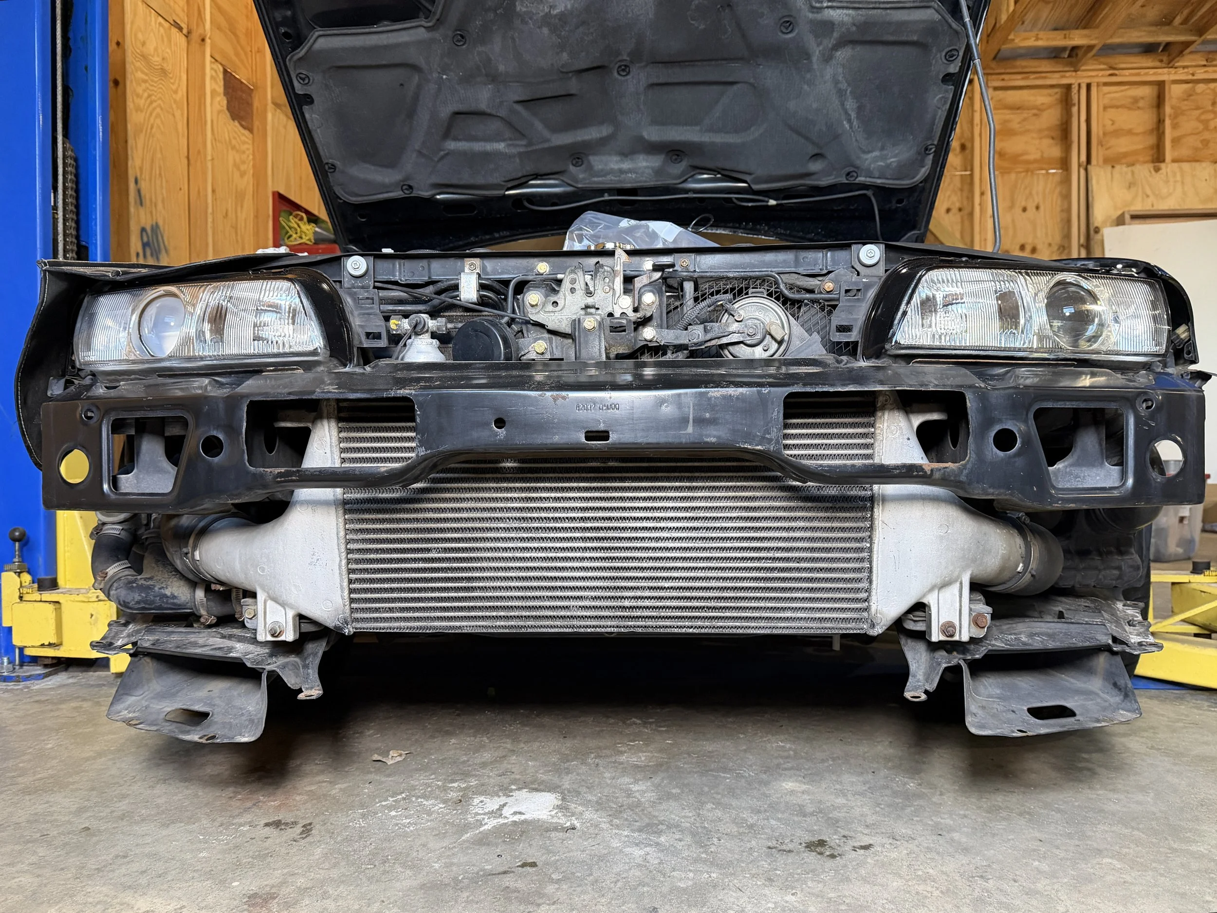 Front view of a car with the hood open, showing the radiator, intercooler, and engine components inside a garage.