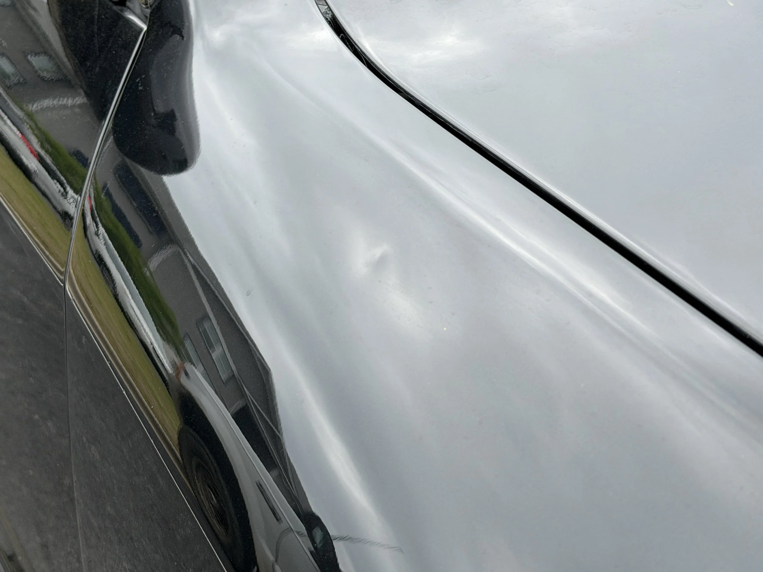 Close-up of a shiny silver car reflecting the surroundings, including a house and a grassy area.