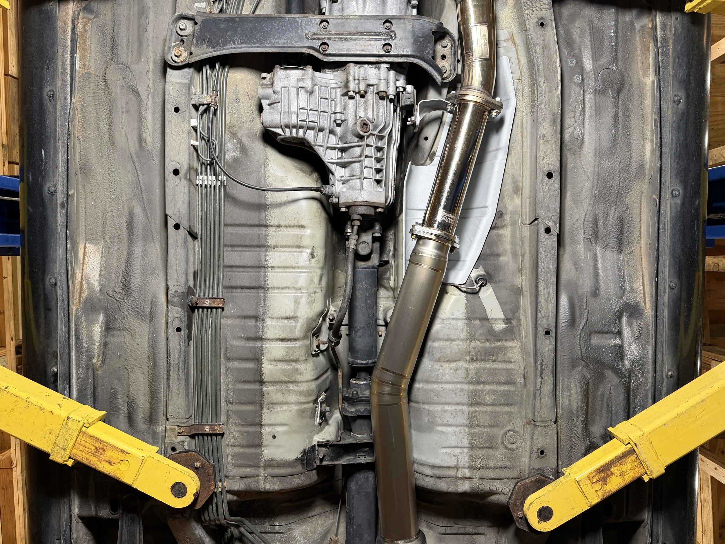 Underbody view of a vehicle showing the exhaust system, transmission, and skid plates, with safety stands supporting the vehicle.