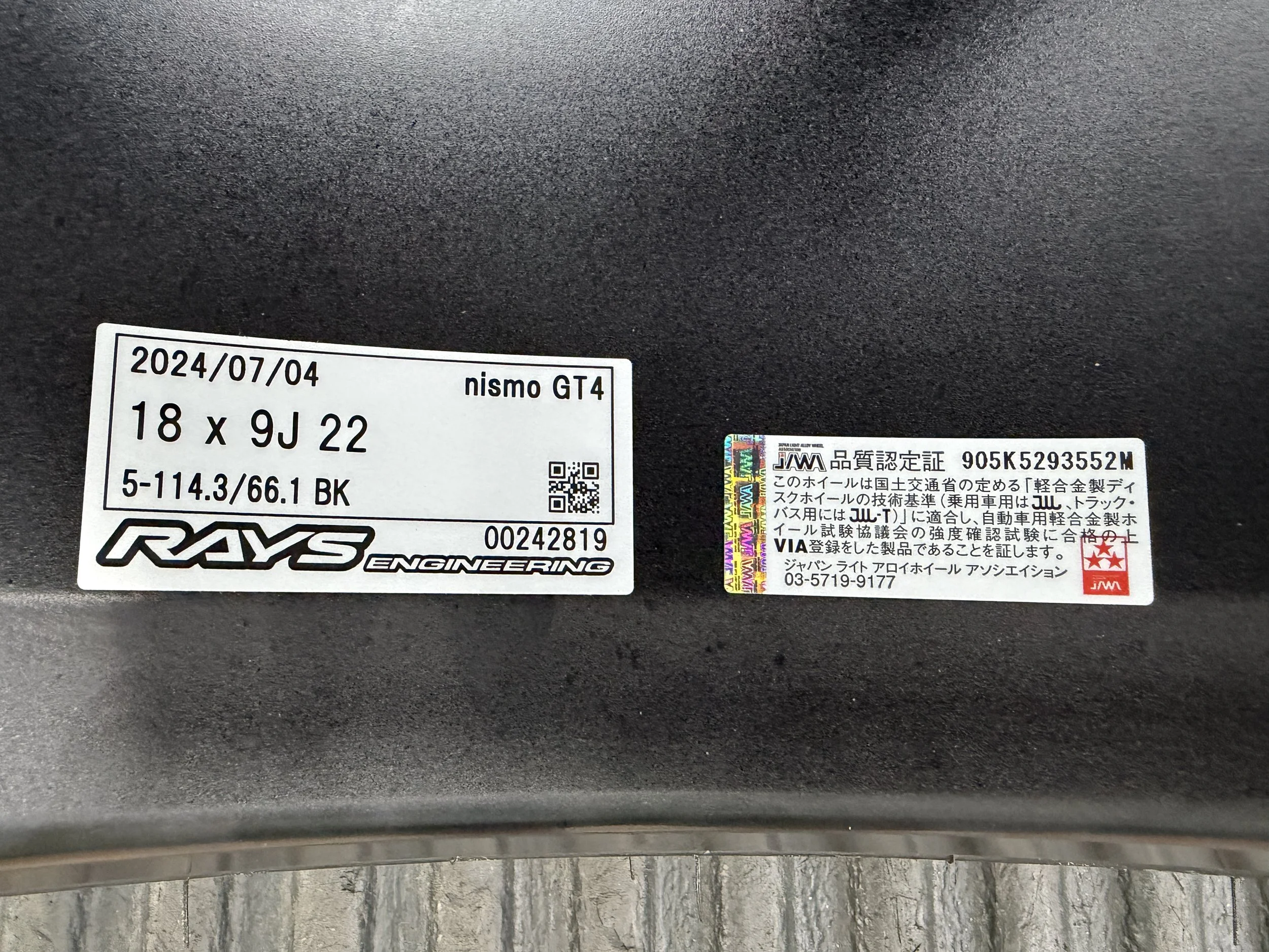 Close-up of a wheel label showing the date 2024/07/04, tire size 18 x 9J 22, and brands RAYS Engineering and Nismo GT4, with Japanese certification and warning labels.