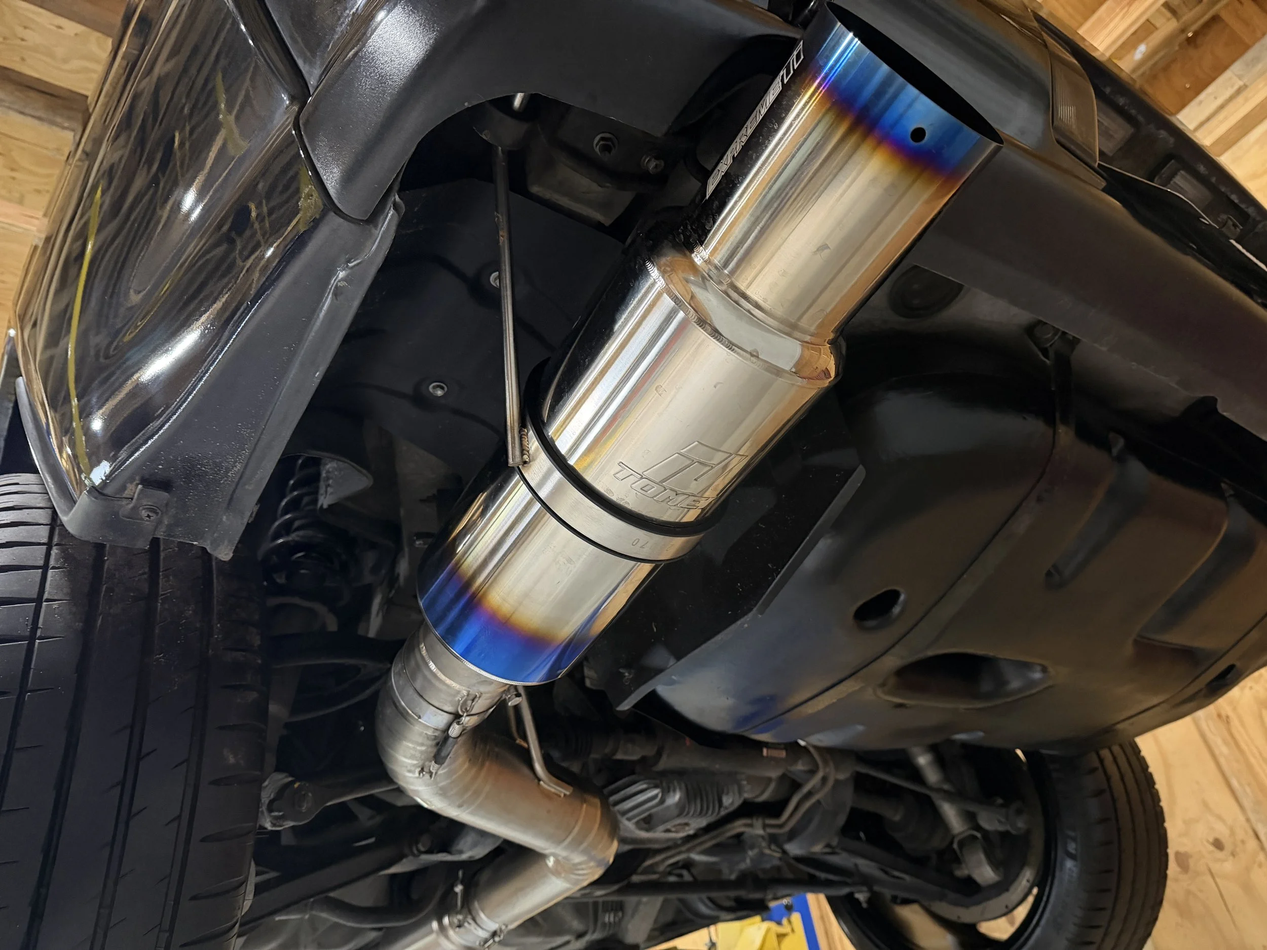 Underneath a car showing a custom exhaust system with a stainless steel muffler and pipes.