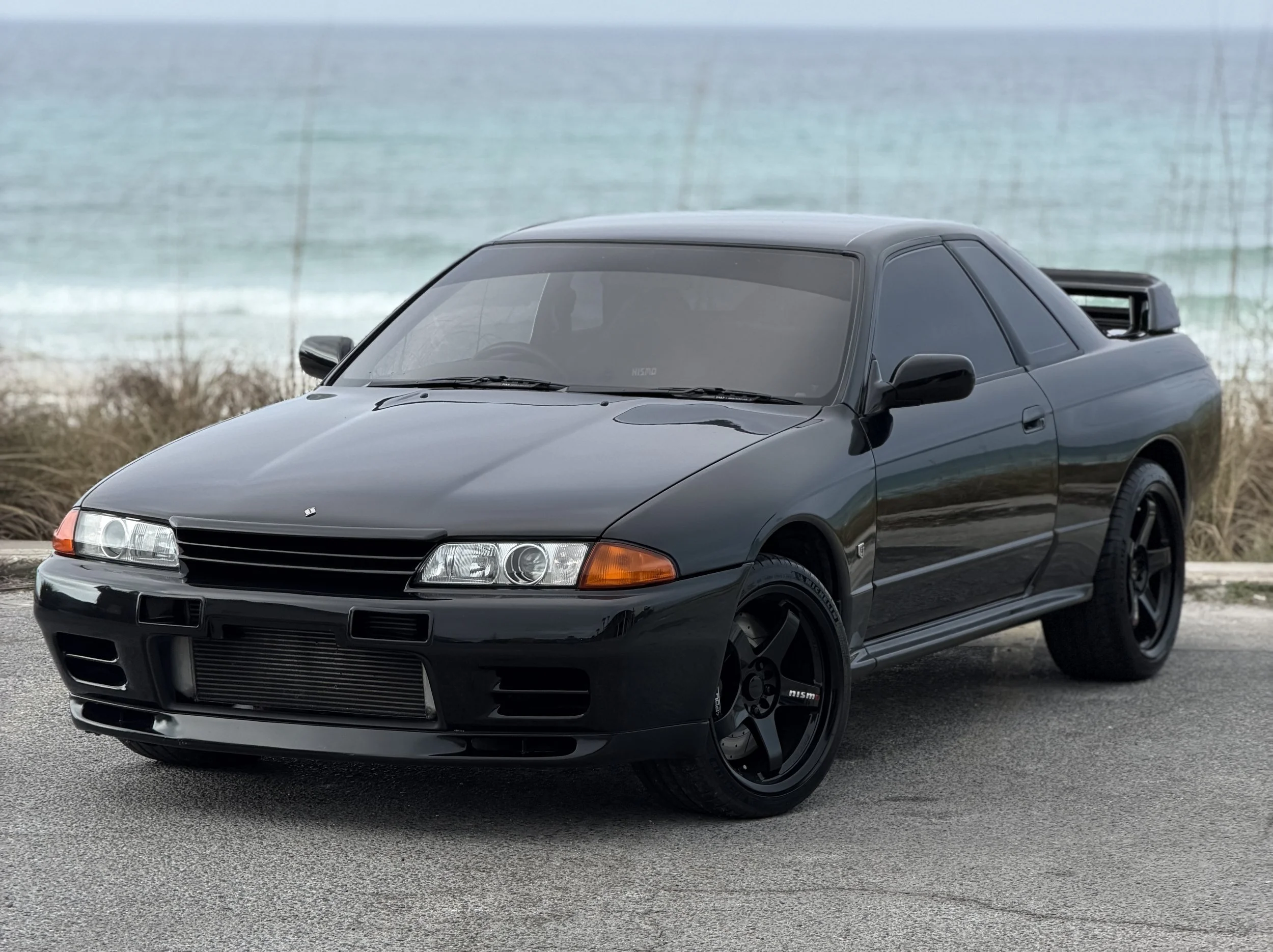 R32 NISSAN SKYLINE GTR FOR SALE
Black Nissan 240SX sports car parked near beach with ocean background.