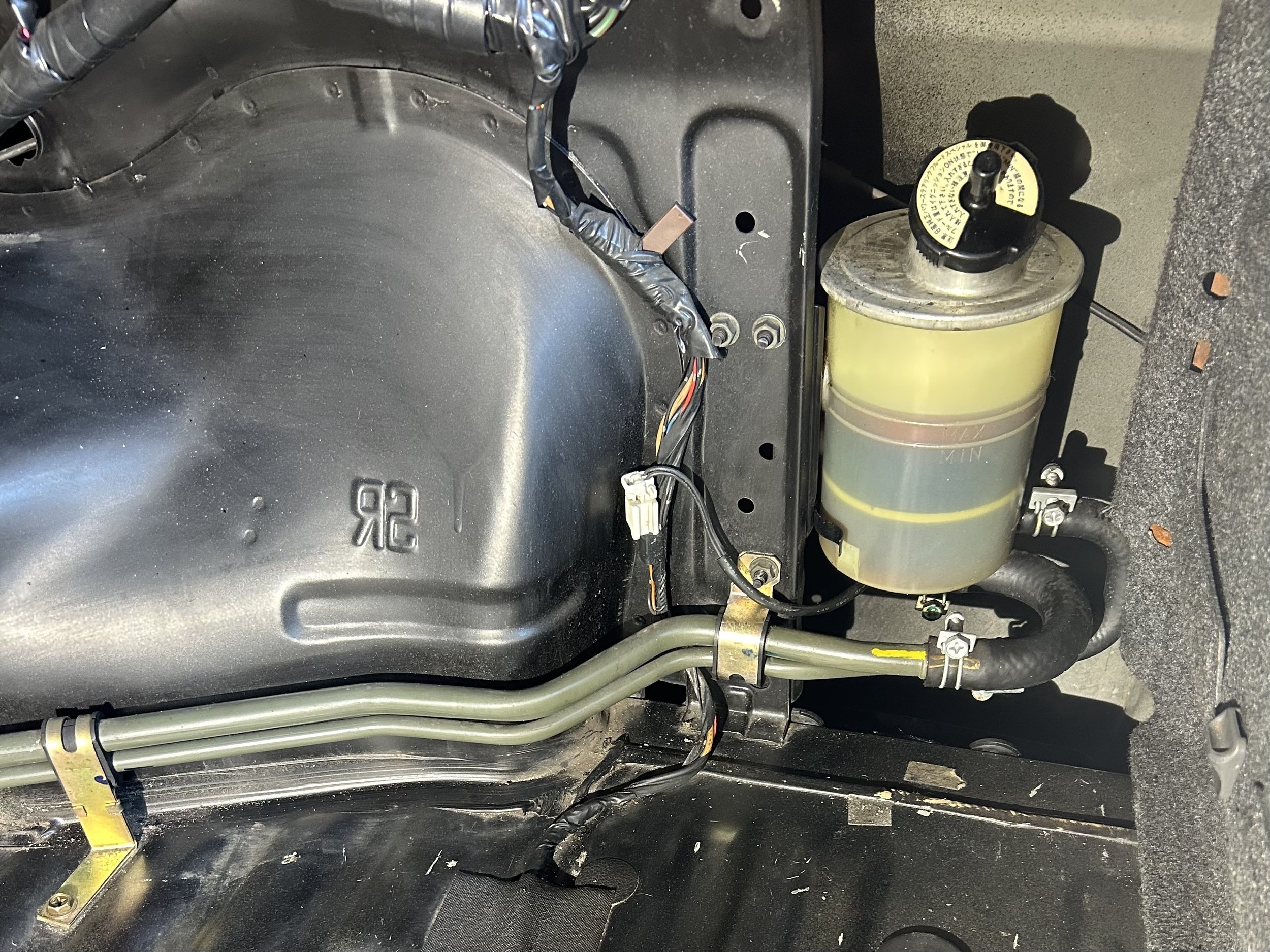 Close-up of a car's interior showing a metal tube, wiring, and a small transparent container with yellow and green fluid.