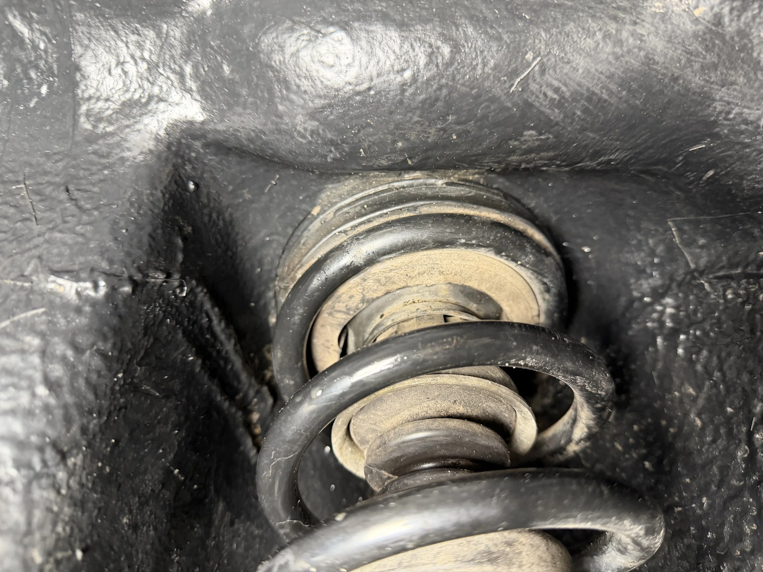 Close-up of a vehicle's suspension coil spring and shock absorber inside a black wheel well.