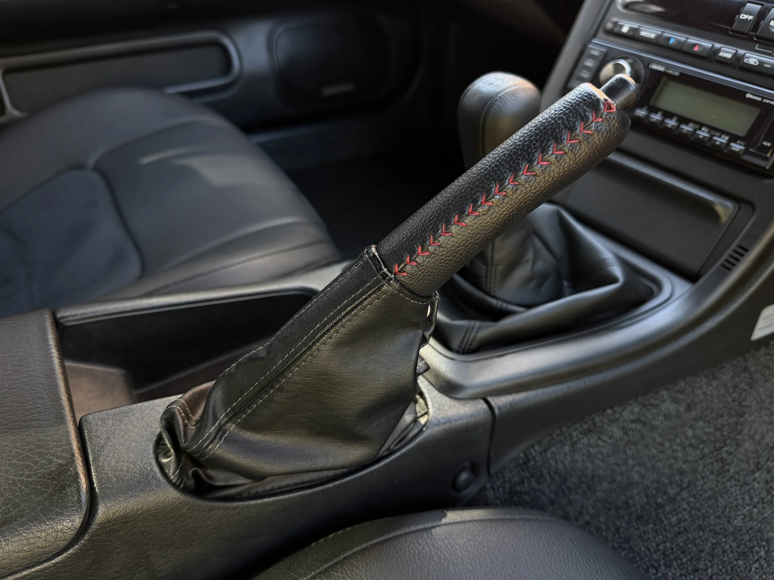 Close-up of a black leather gear shift knob with red stitching in a car interior.
