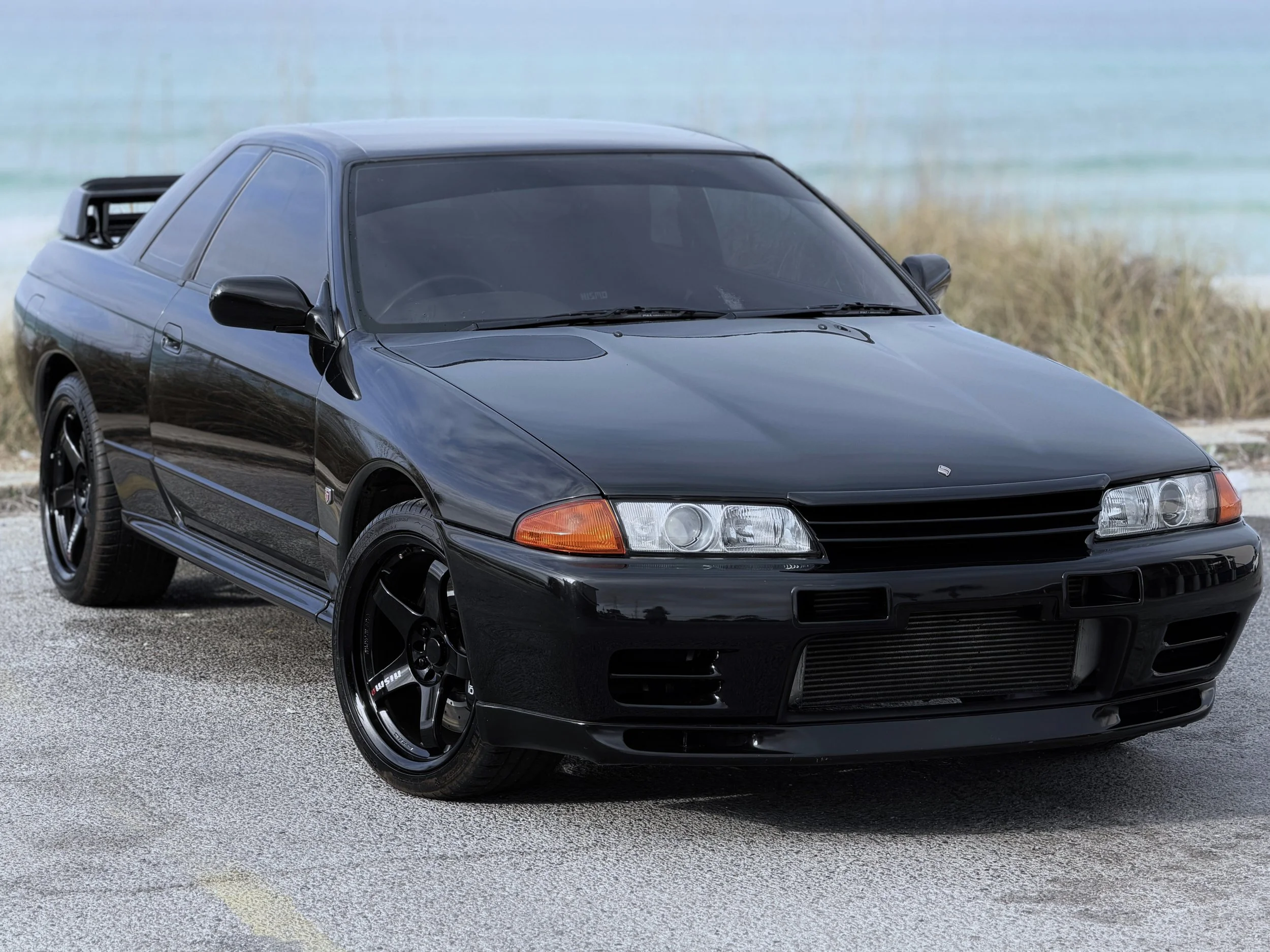A black sports car parked on a gravel area near water and some plants.