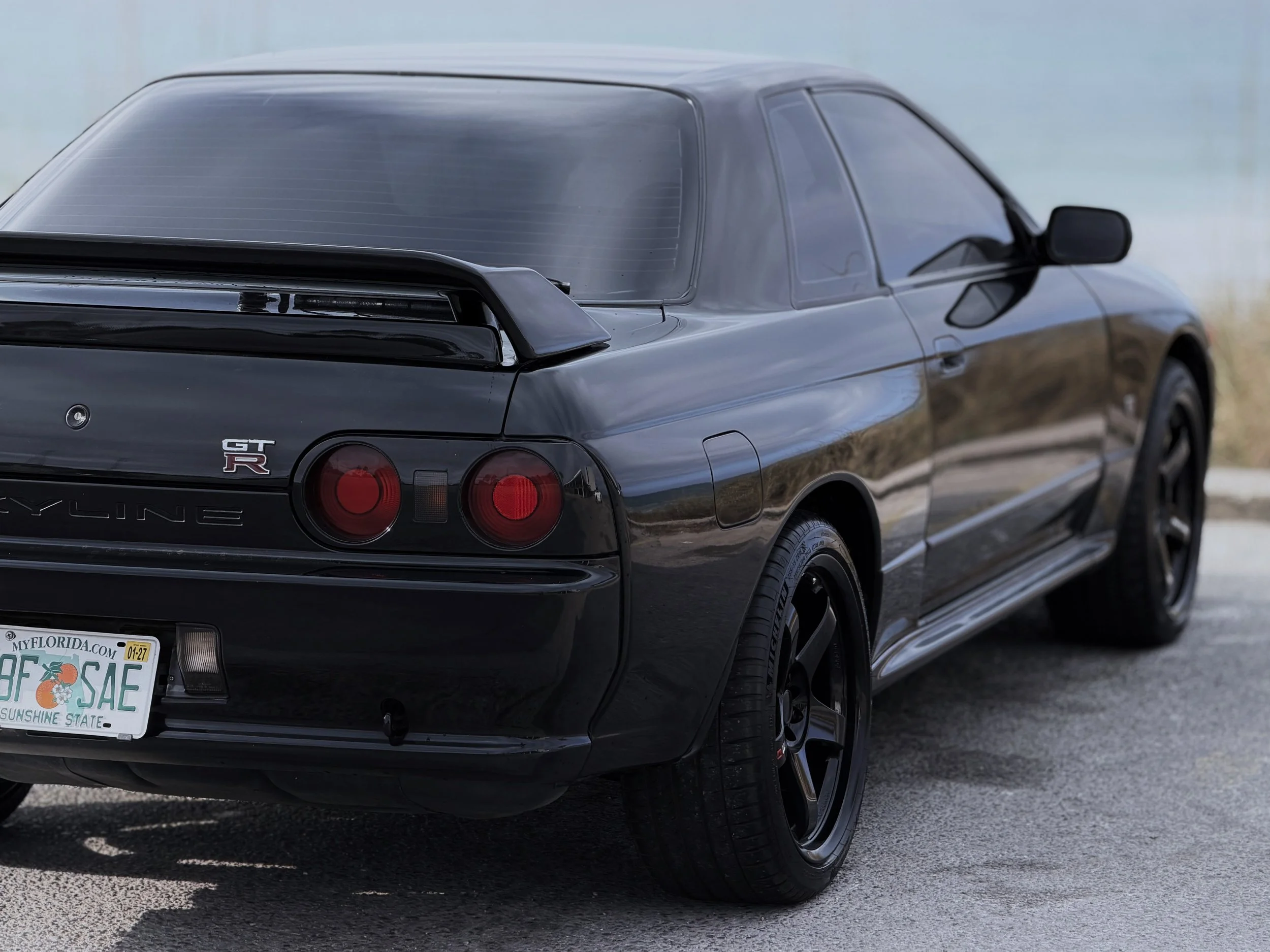 Black Nissan GT-R car parked on a road, showing the rear and side view with a clear sky background.